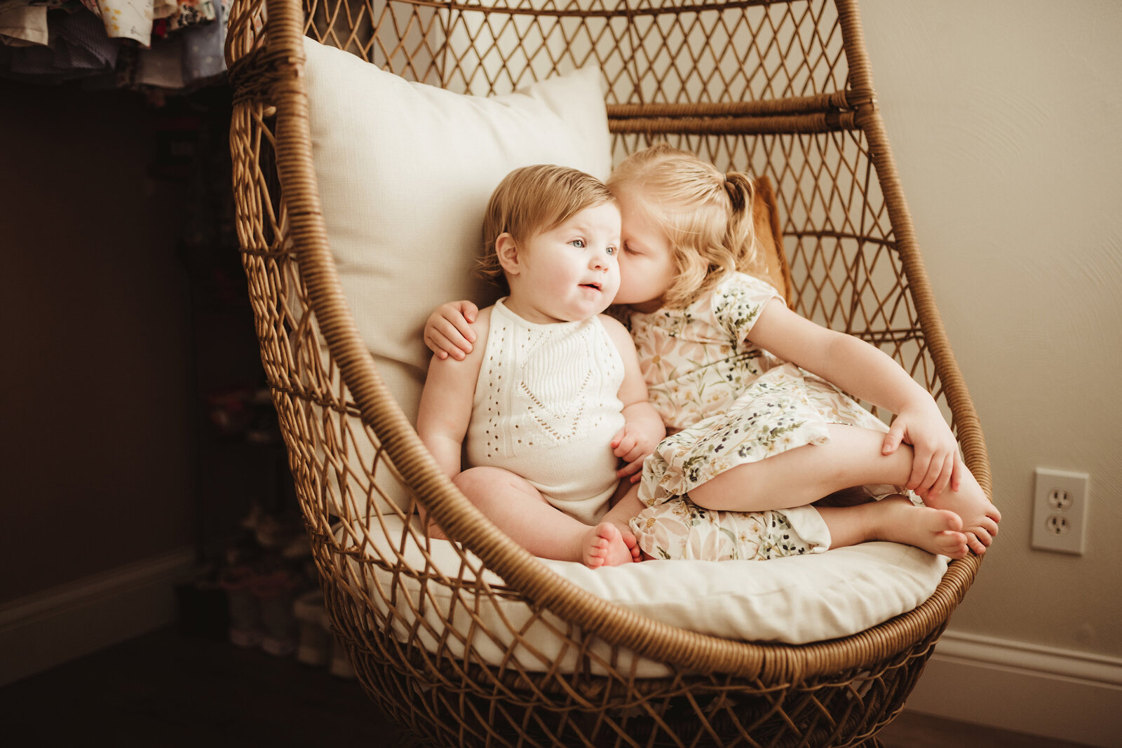 Two little girls sitting together in a wicker chair.