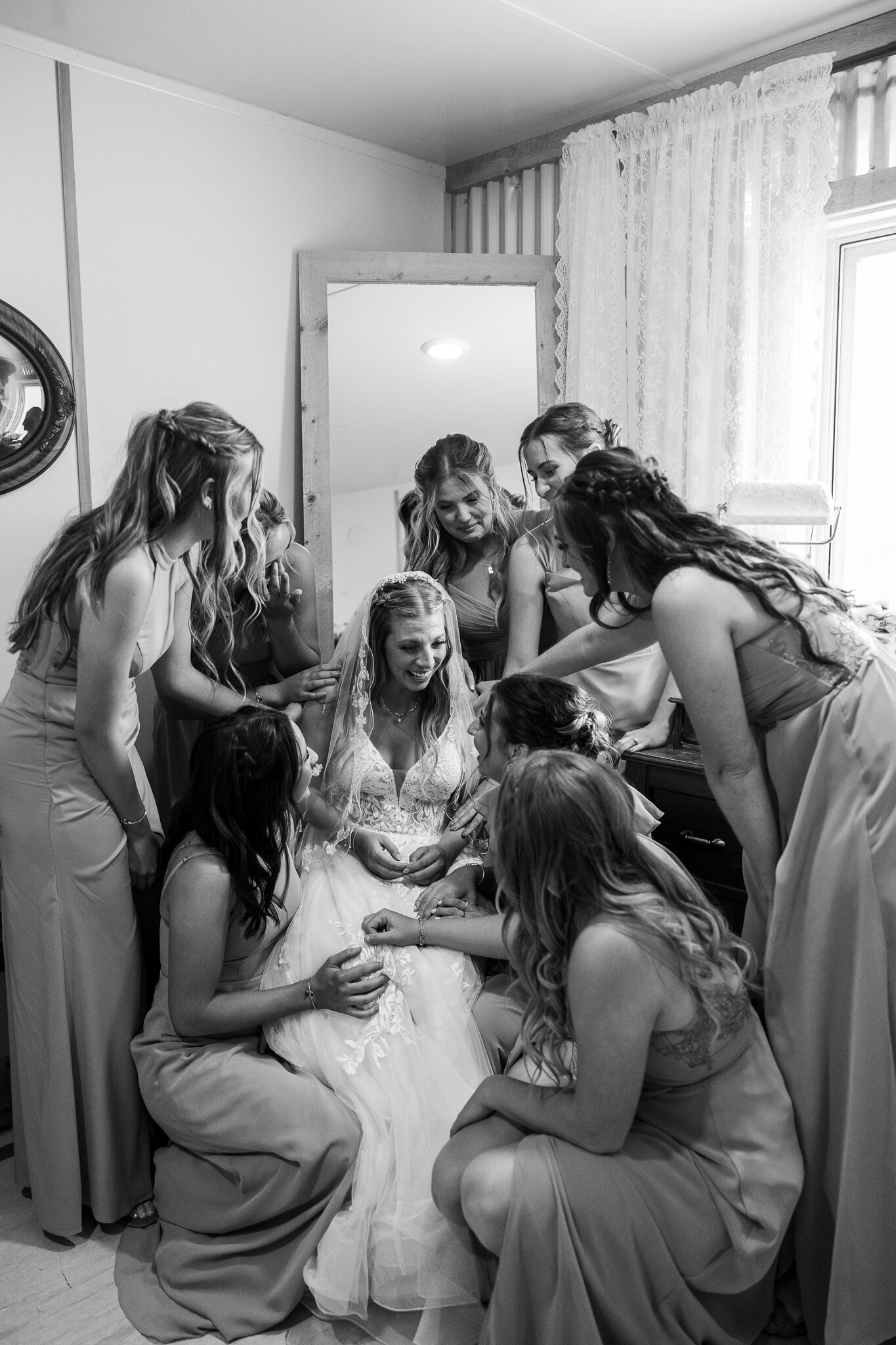 Candid black and white photo of bridesmaids gathered around the bride before the ceremony at Absolute Prestige in Loma, Colorado.