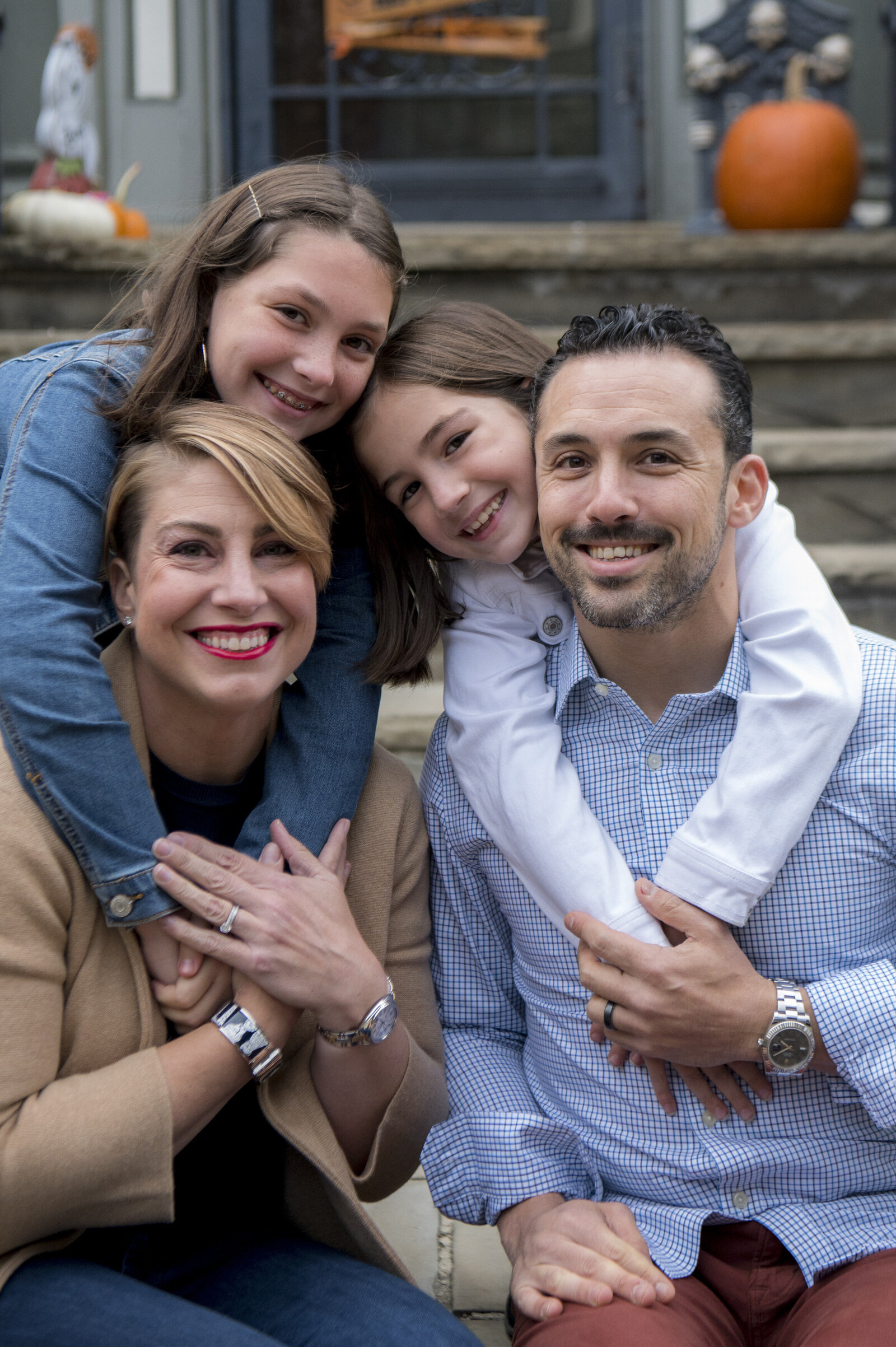Two kids hanging on the back of their parents as they all smile 