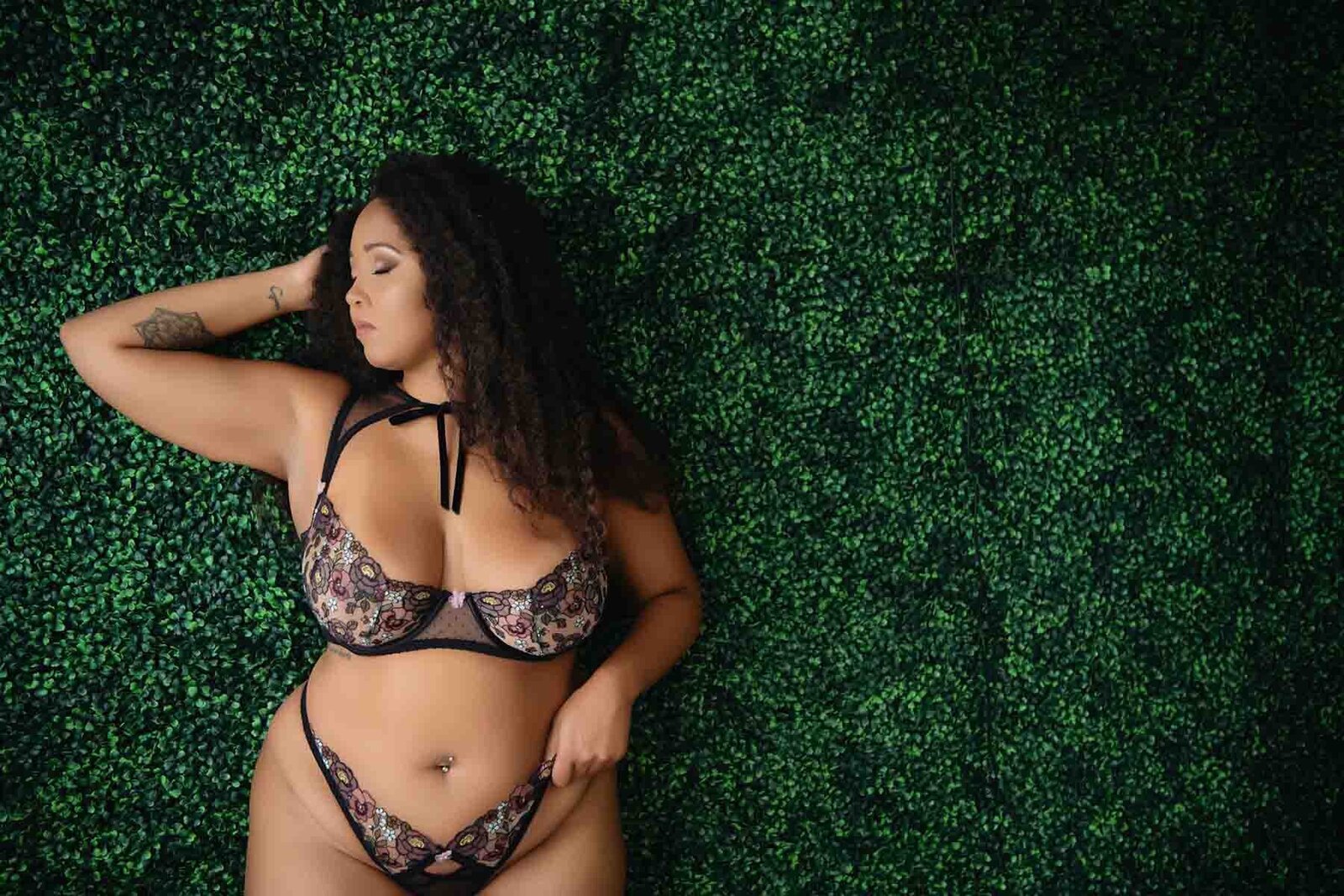 Curvy mixed woman posing against wall of green foliage  for boudoir portrait