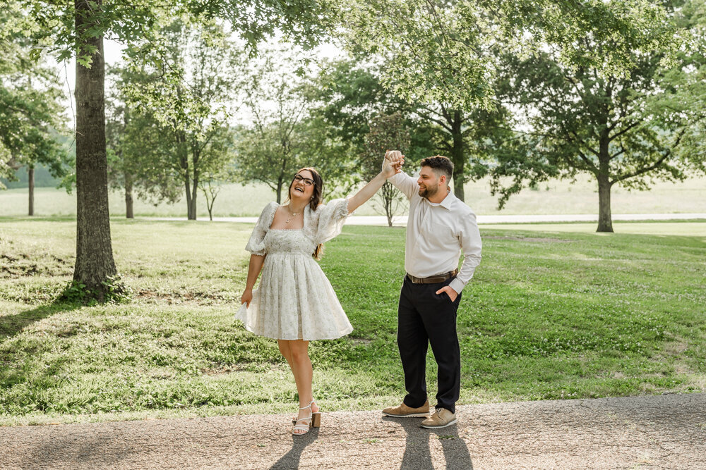 Man playfully twirling his fiancé near a grove of trees