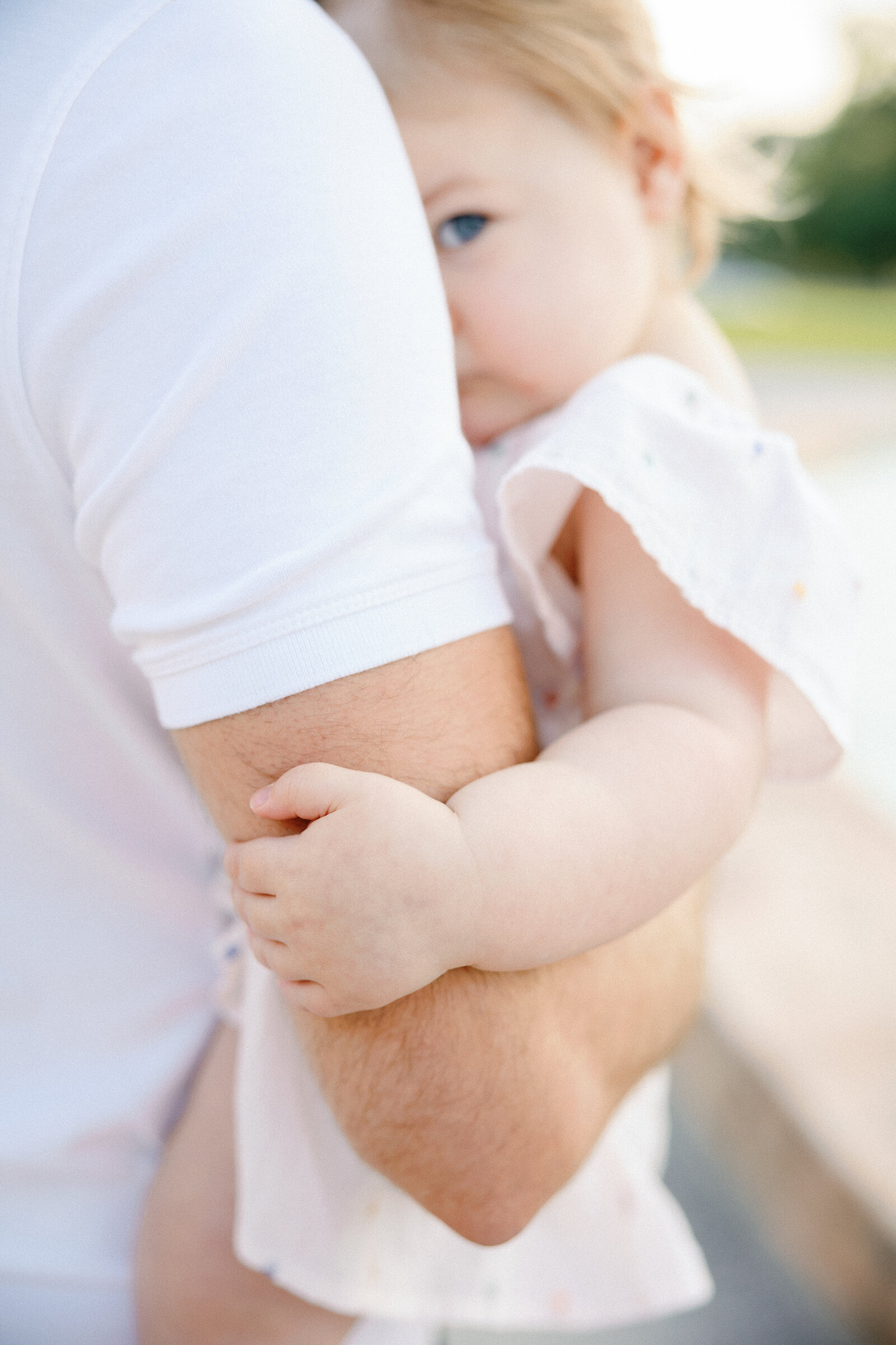 little girl peeking at the camera behind daddy's arm