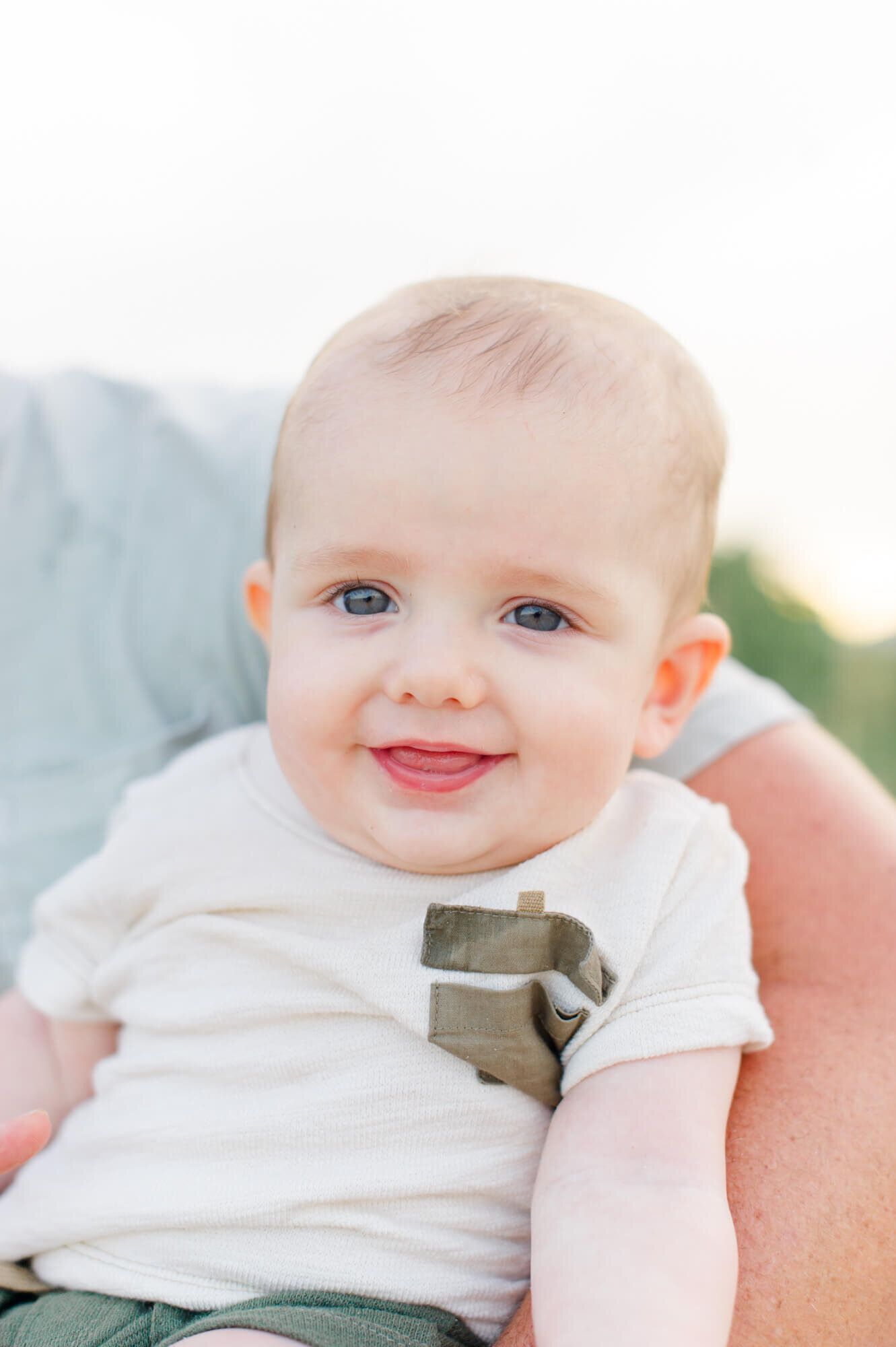 Closeup of a blue eyed baby boy smiling into the camera at sunset