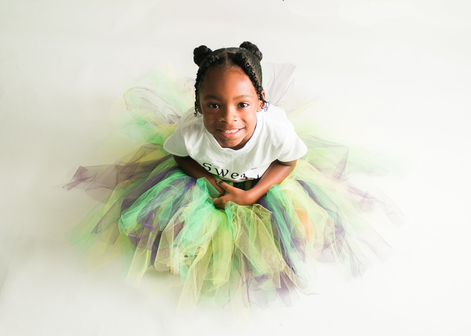 little girl in green and purple tutu  looking up at camera