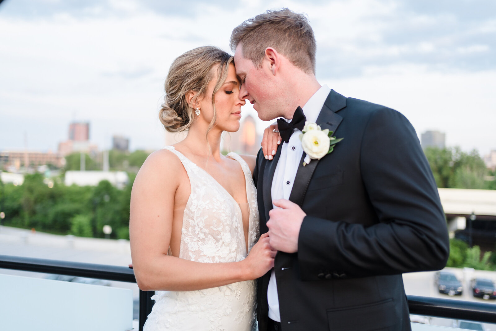Bride and groom lean in and touch foreheads on the balcony at the Fives overlooking the Columbus skyline