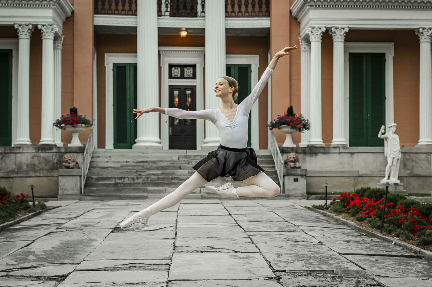 Girl in ballet attire elegantly leaping in front of a building
