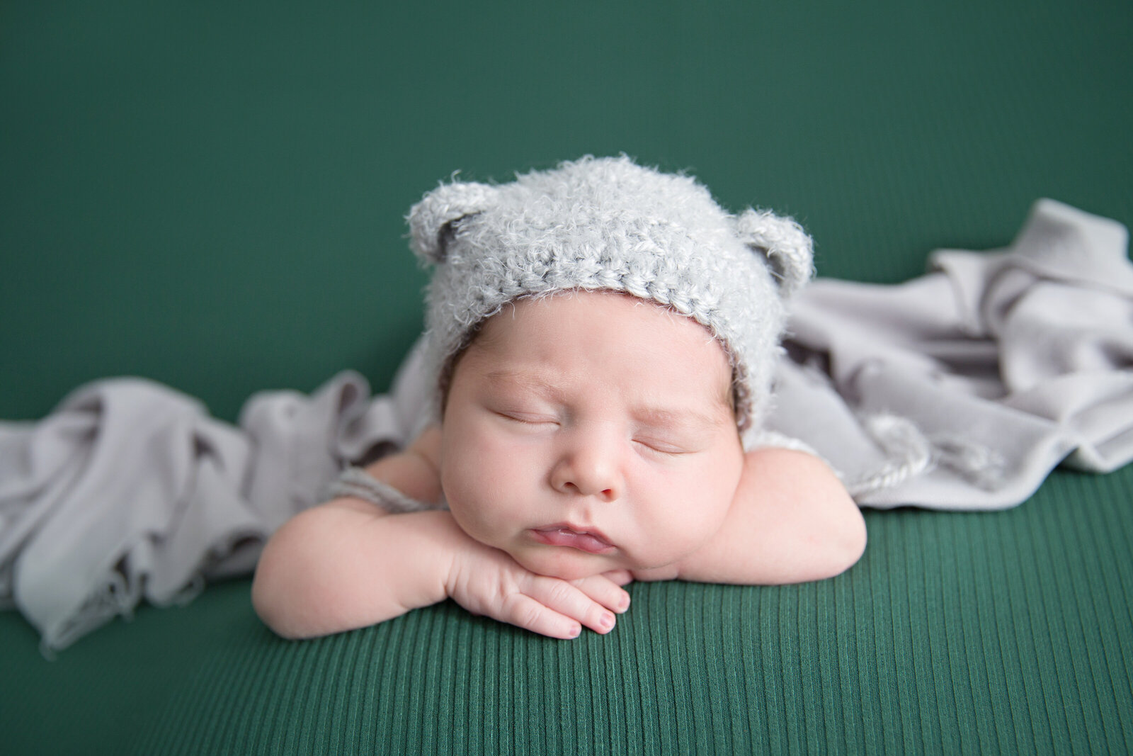 sleeping newborn wearing grey bear hat posed on green fabric