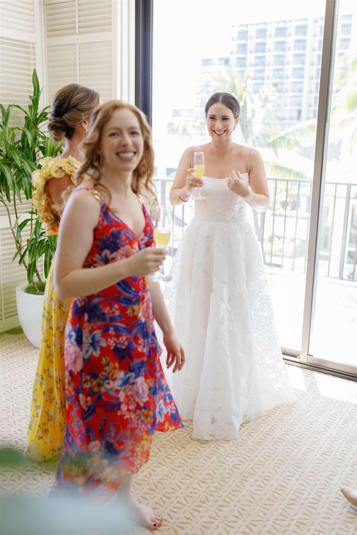A newlywed in a dress holding a champagne glass and laughing with their bridal party 