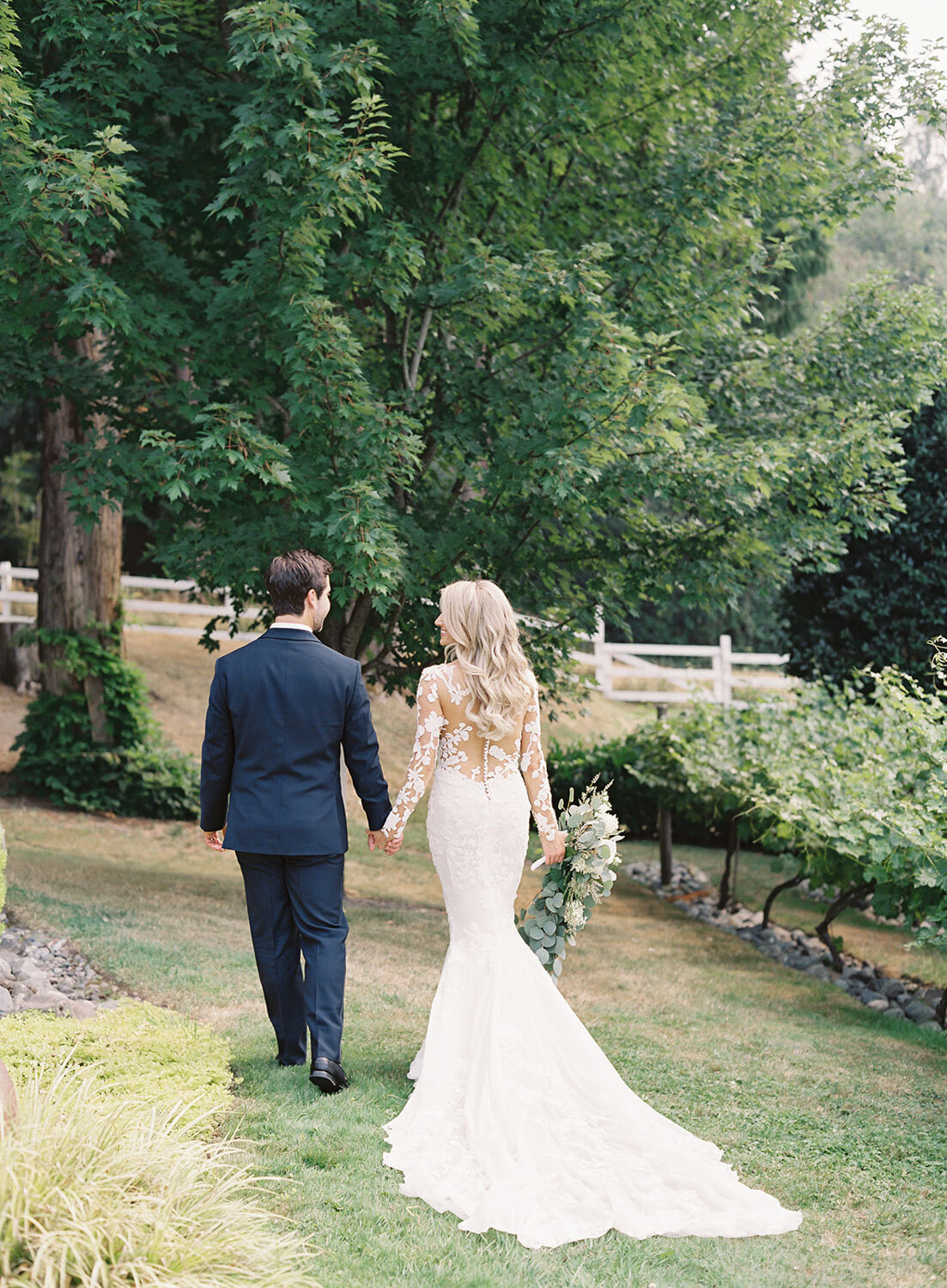 Bride and groom walking hand in hand through a garden.