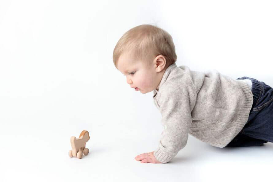 Baby crawls toward a toy in a white photo studio.