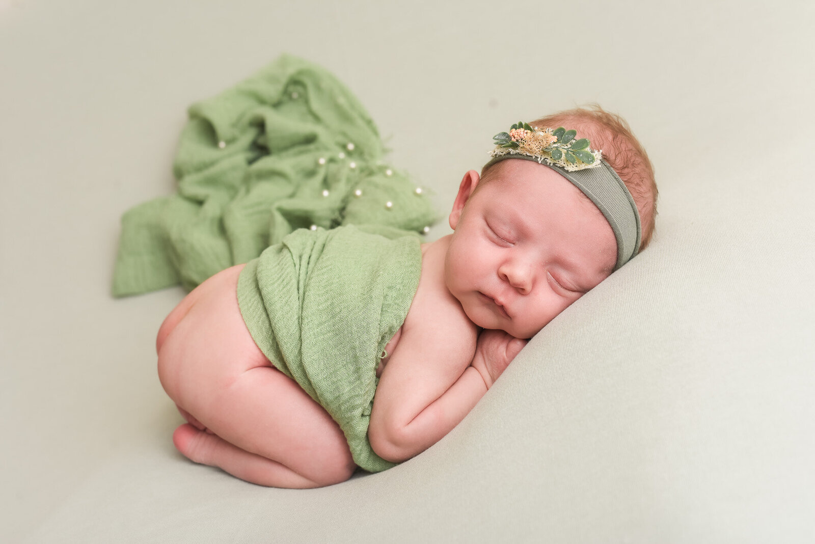 newborn baby laying on her stomach with green head band on and green blanket