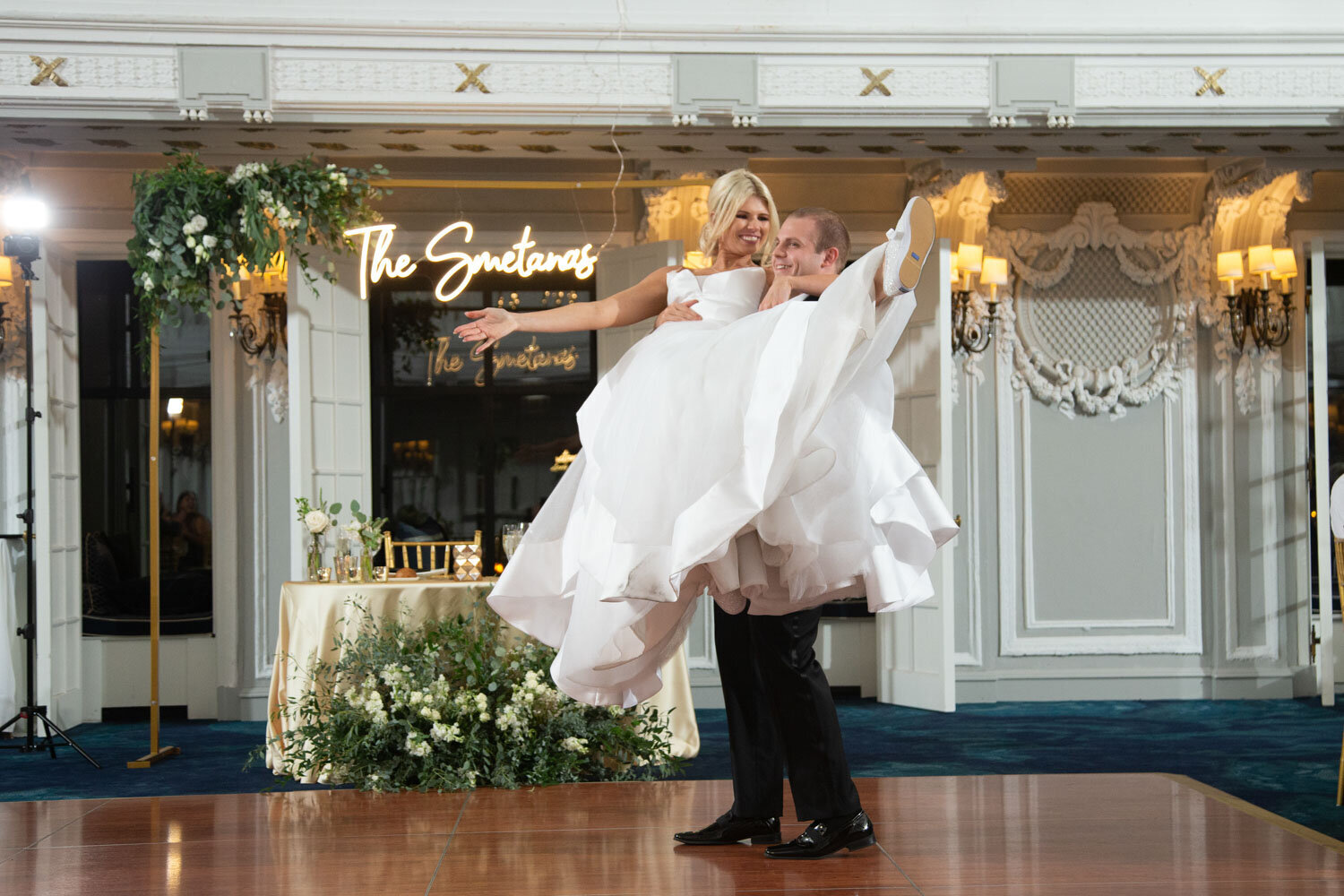 A bride and groom are dancing in front of a neon sign