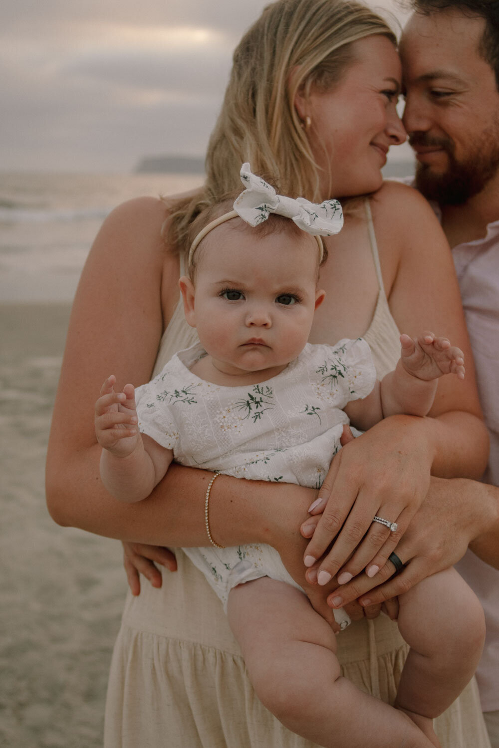 Baby girl held by her parents, with the beach in the background