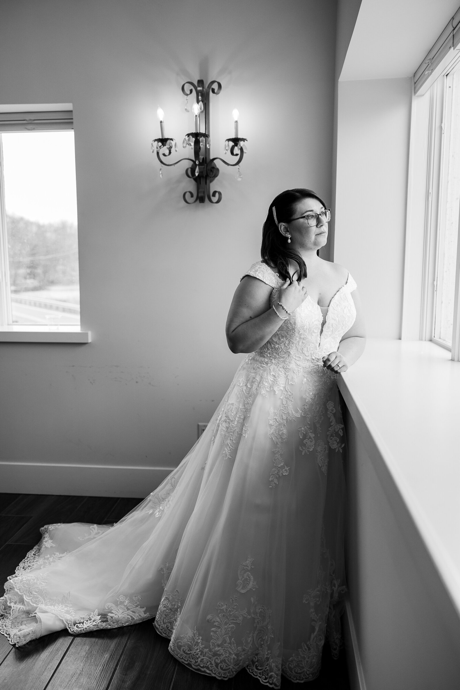 Black and white photo of bride looking out the window in a quiet moment before her Perona Farms wedding