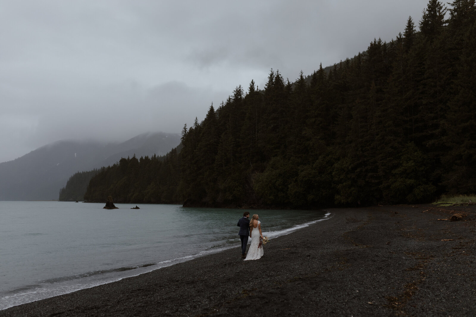 Bride and groom walking on rainy beach with umbrella