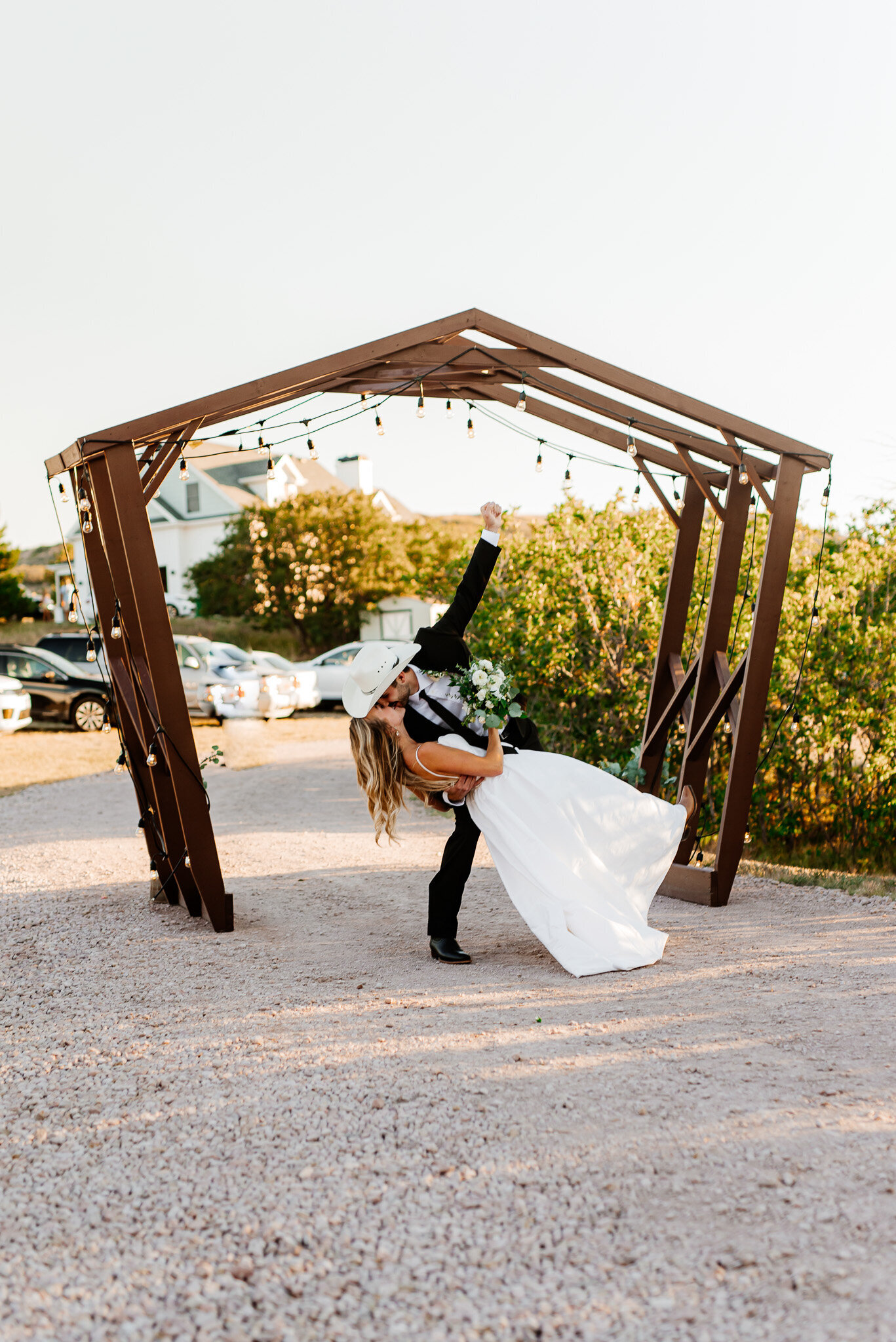 groom with a cowboy hat dips his bride for a kiss