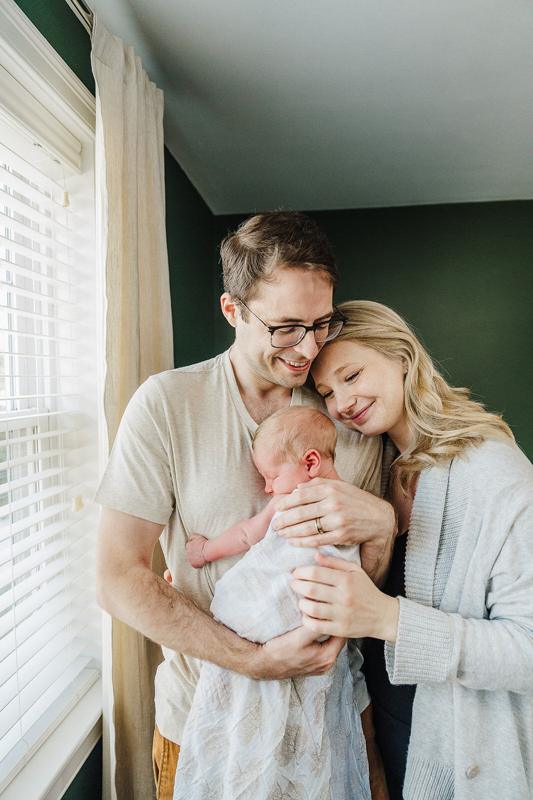 parents snuggle newborn baby against a green wall