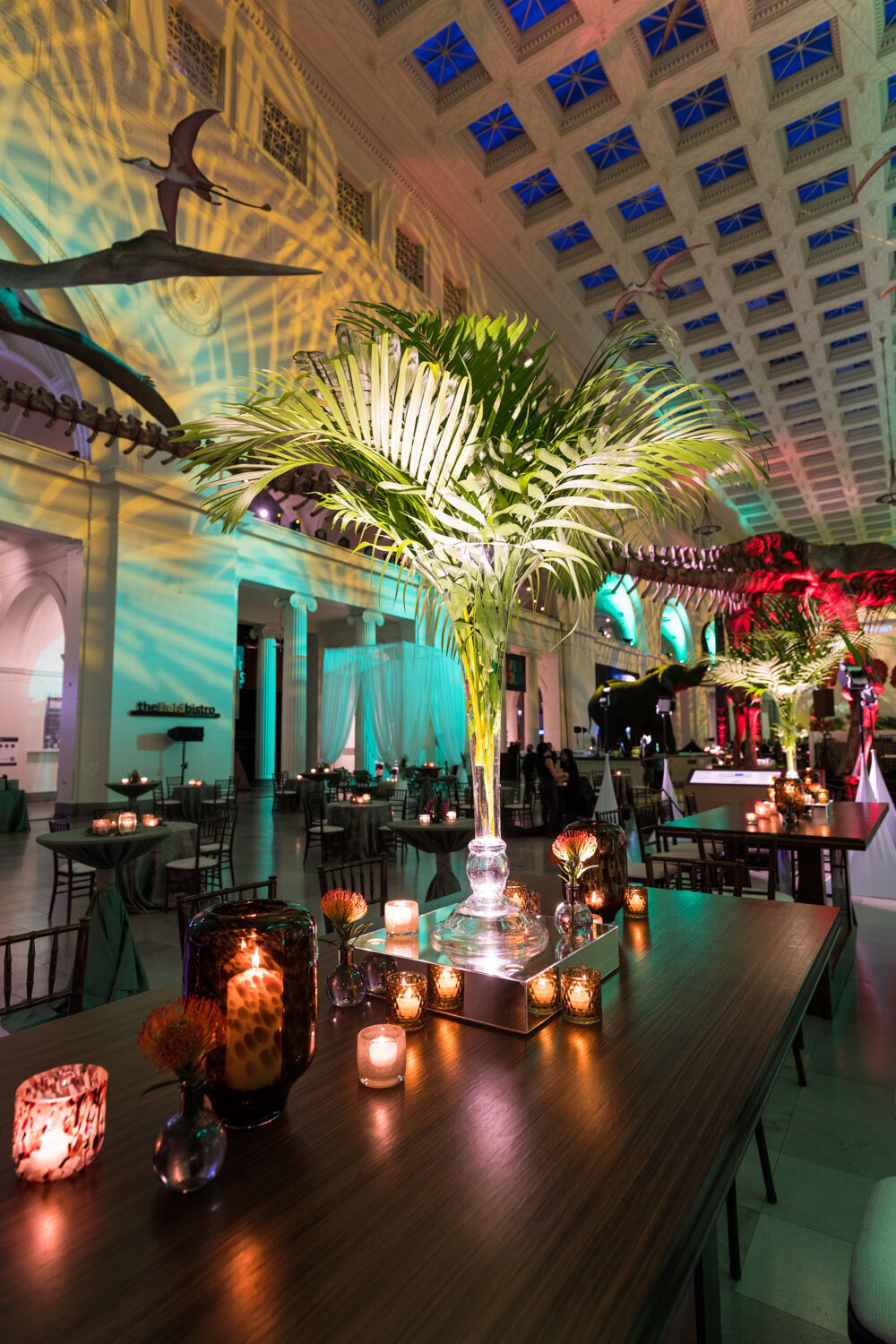 Tall palm centerpieces with candles in an event hall with dinosaur decor