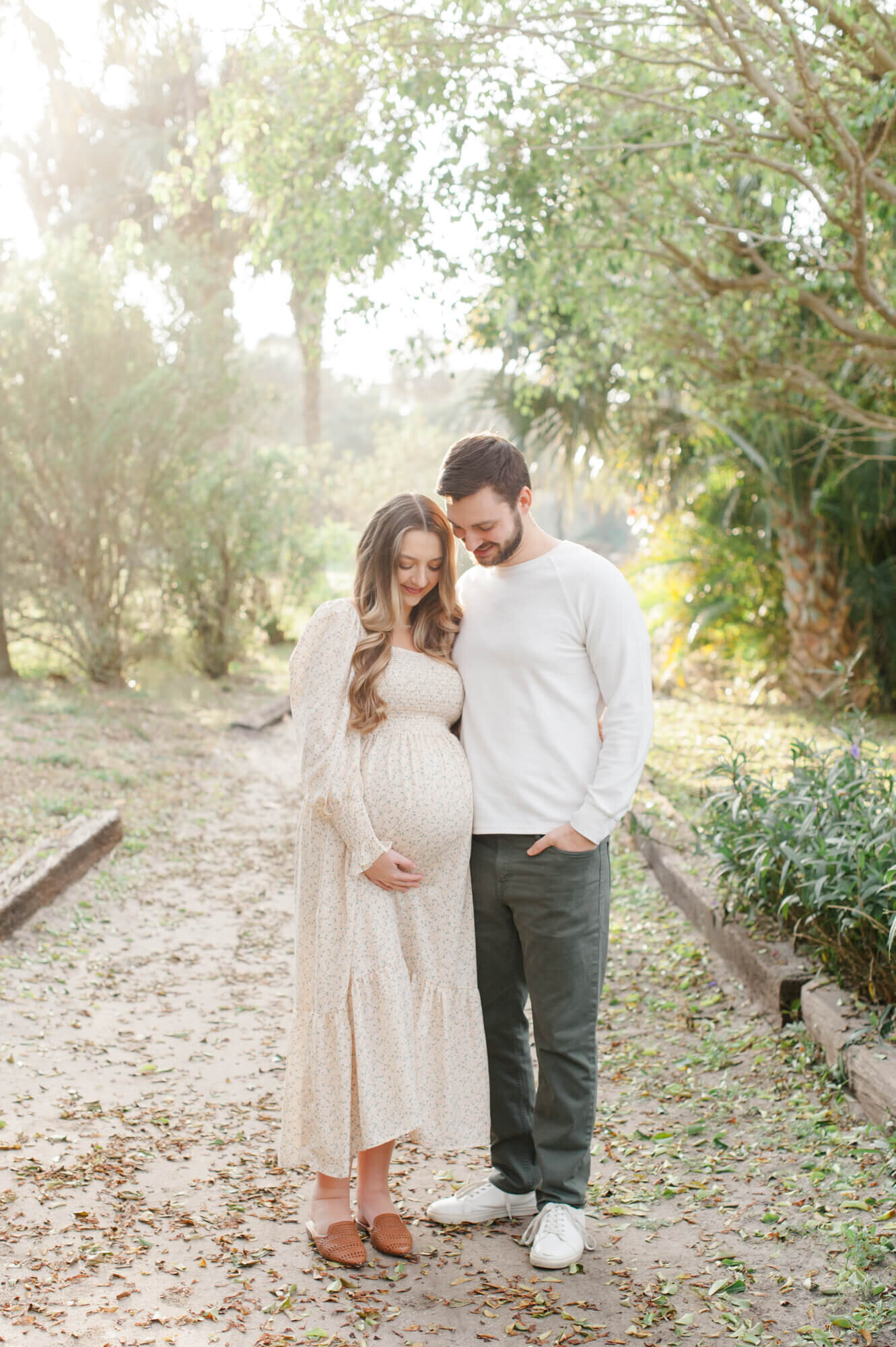 Pregnant couple look towards the moms belly while standing on a beach access