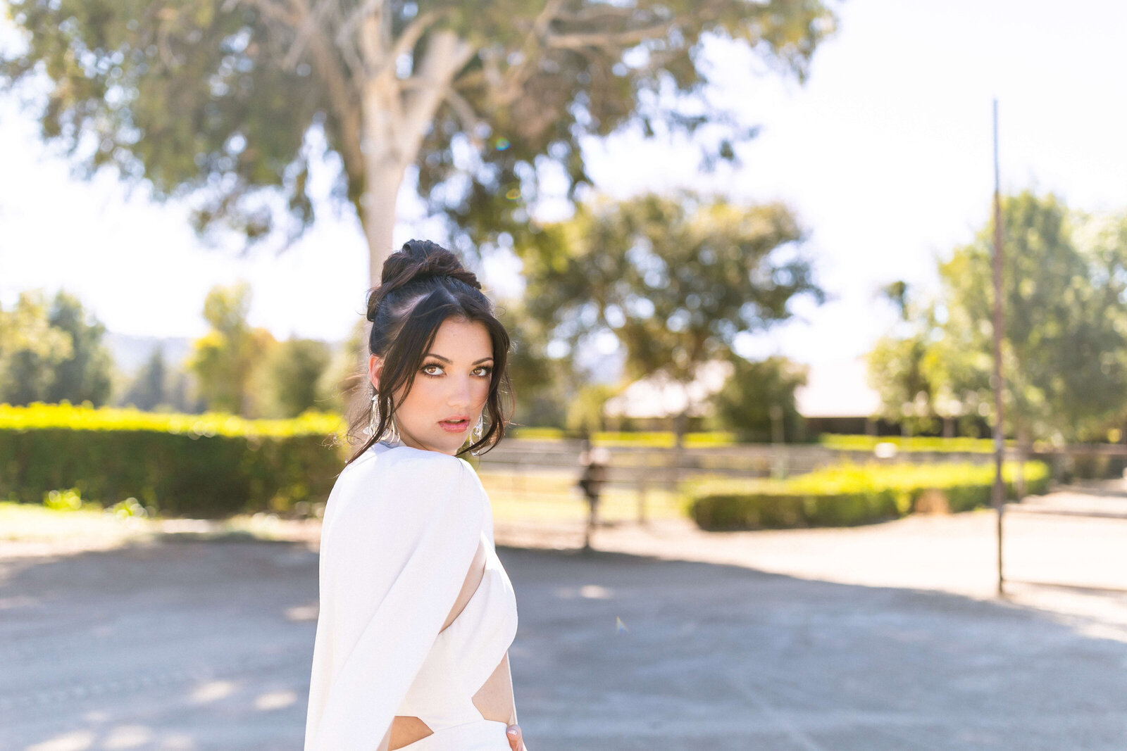 girl with dark hair doing a model pose in an all white outfit in a park