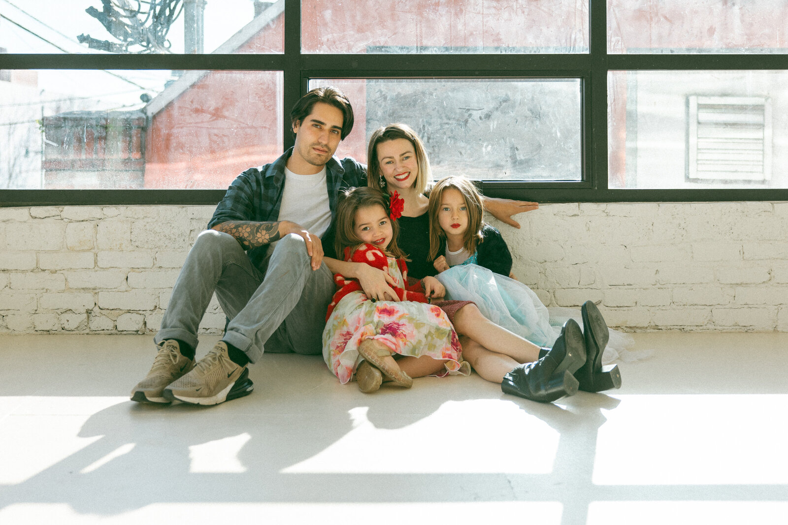 family of four cuddled up and sitting on floor in front of large windows in photo studio