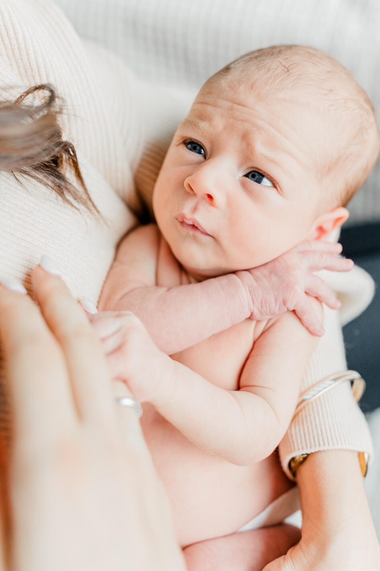 Newborn grasps mom's finger and looks up at her