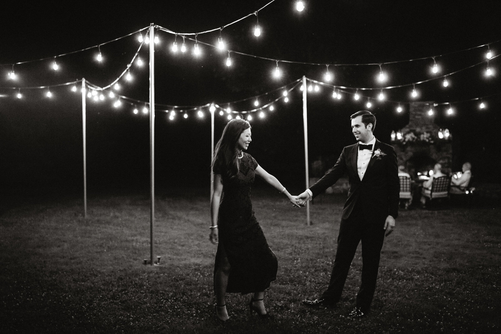Bride and groom share a romantic moment  under the lights behind the Inn at Fernbrook Farm.