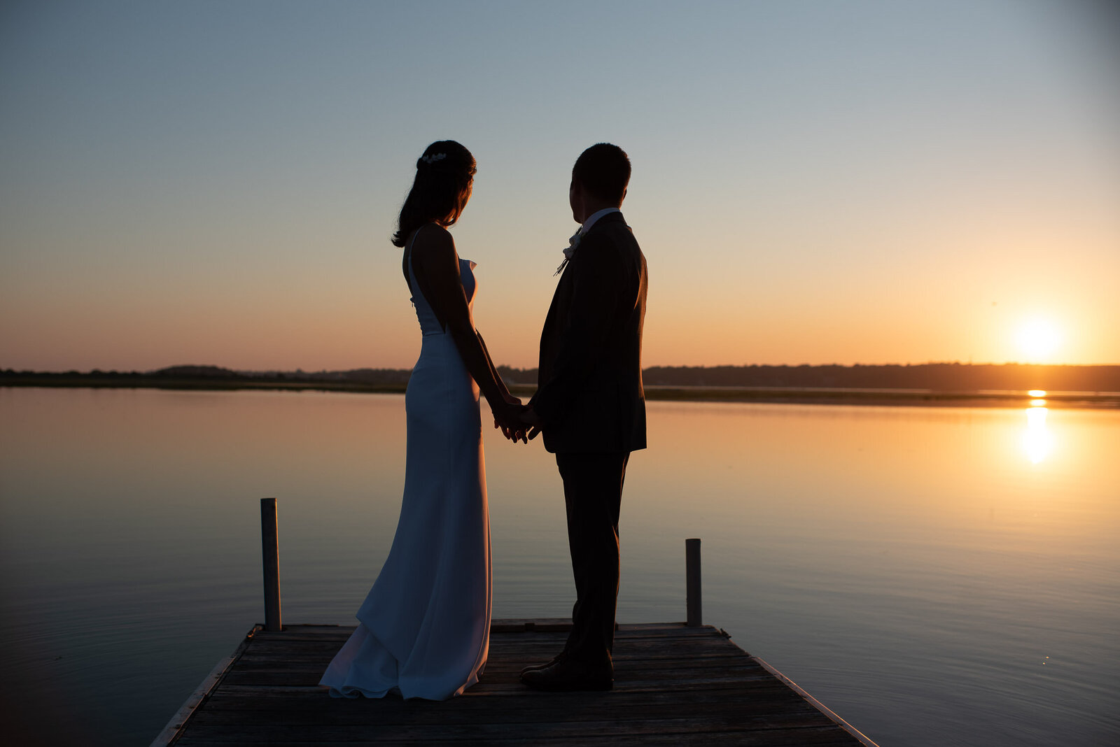 bride and groom silhouette on dock at twilight