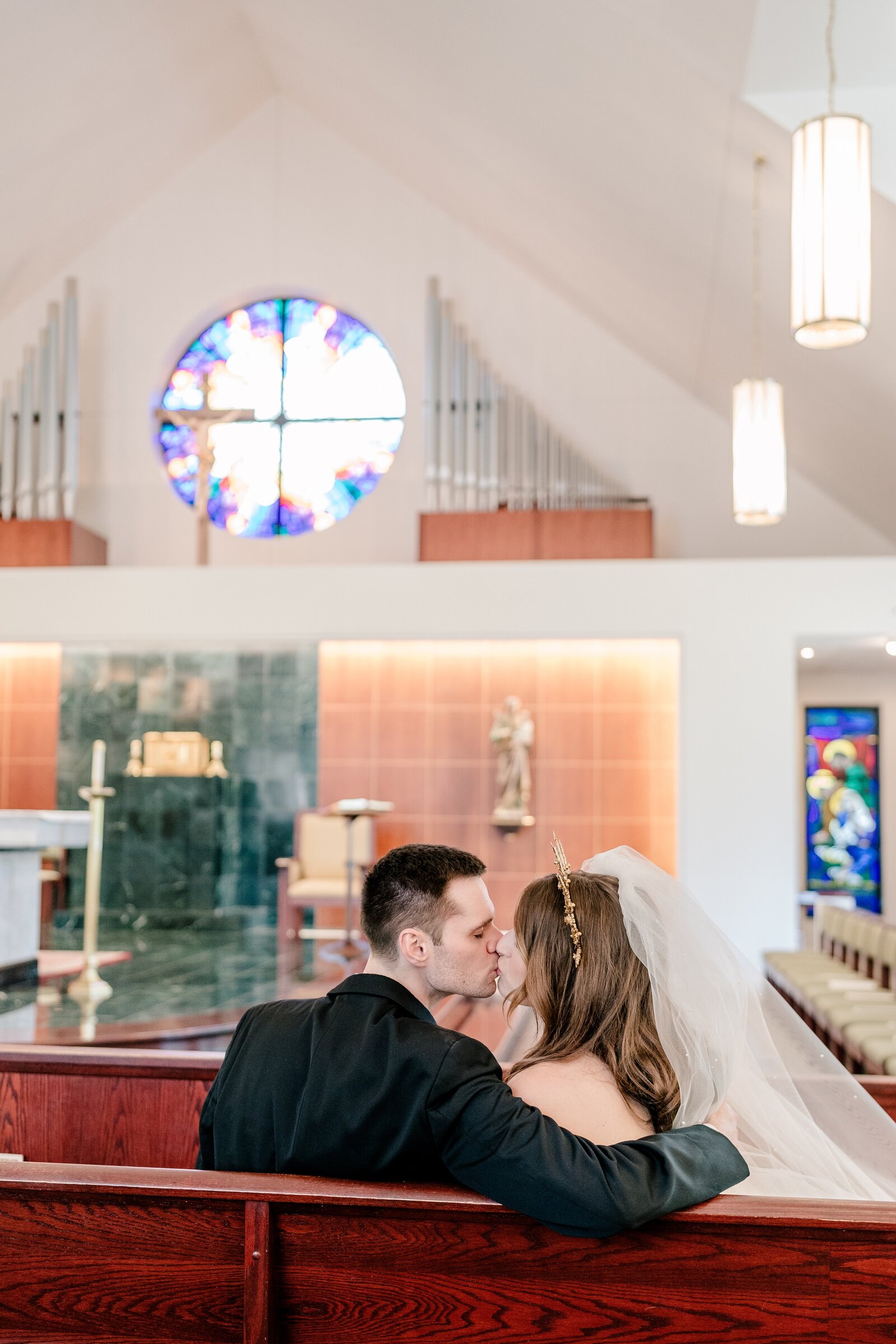 A bride and groom share a kiss after their Catholic wedding at the St. Robert Bellarmine Chapel at George Mason University