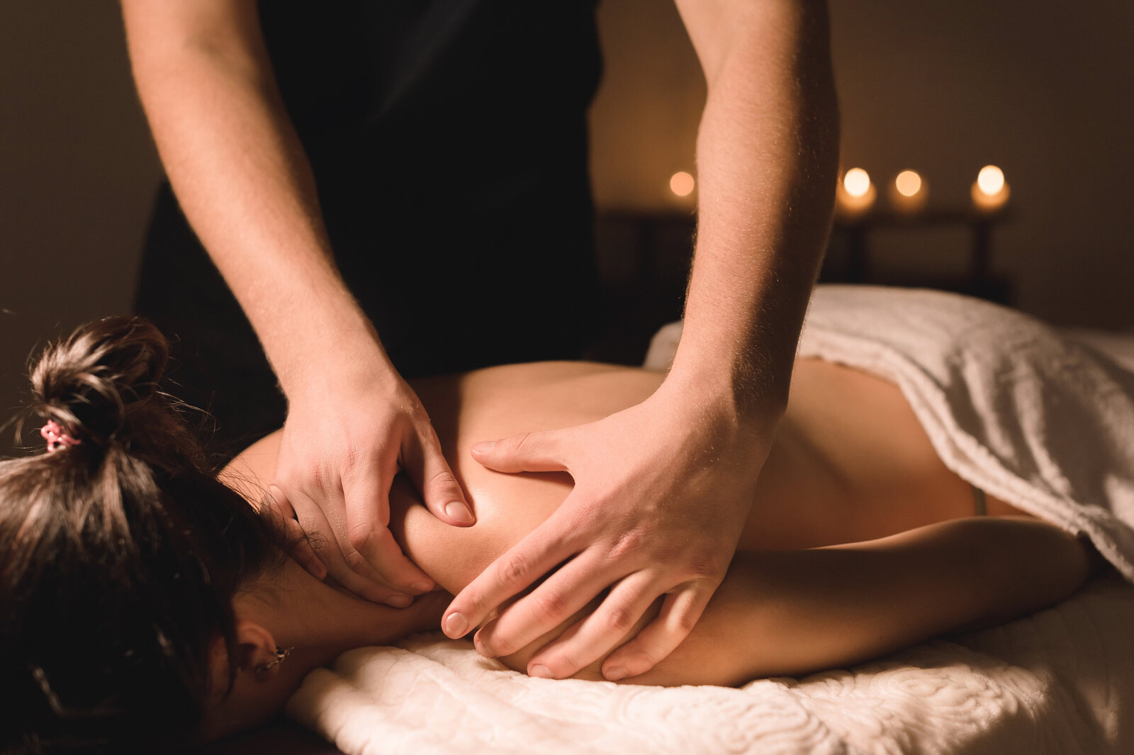 Massage therapist applying relaxing shoulder pressure in a softly lit room, supporting stress relief for caregivers.