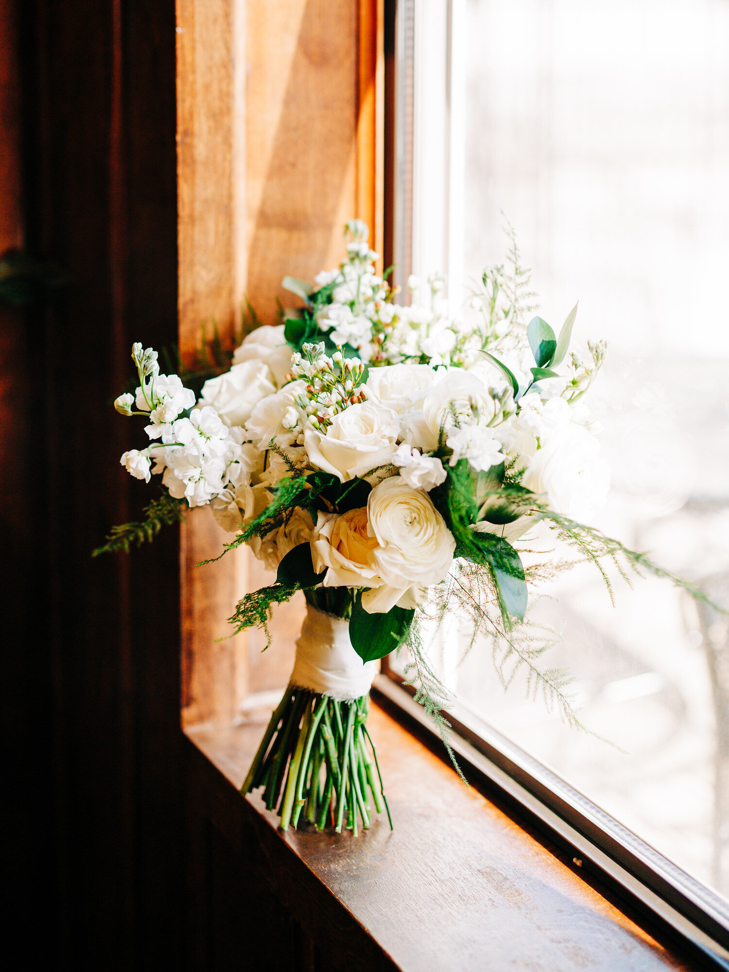 This image, taken by Austin wedding photographer KD Captures, features a white floral bouquet with baby's breath and white roses paired with other greenery. The bouquet is propped up on a windowsill.
