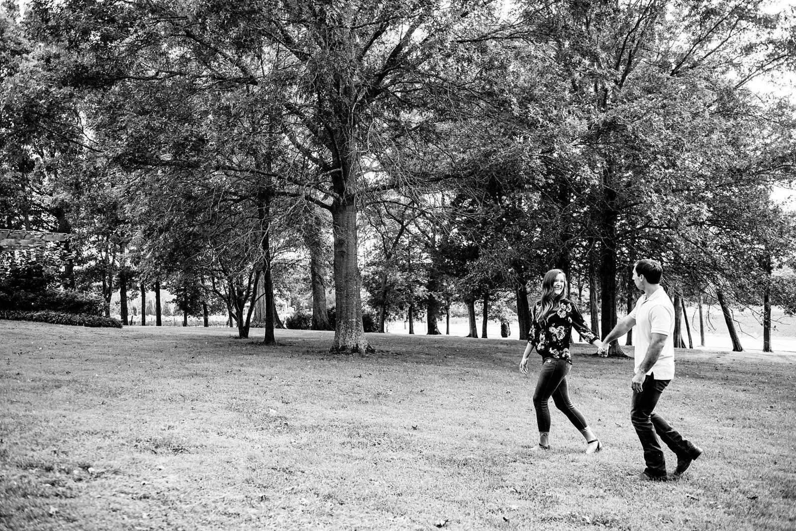 Black and White photo of couple walking in a park together, she is leading him
