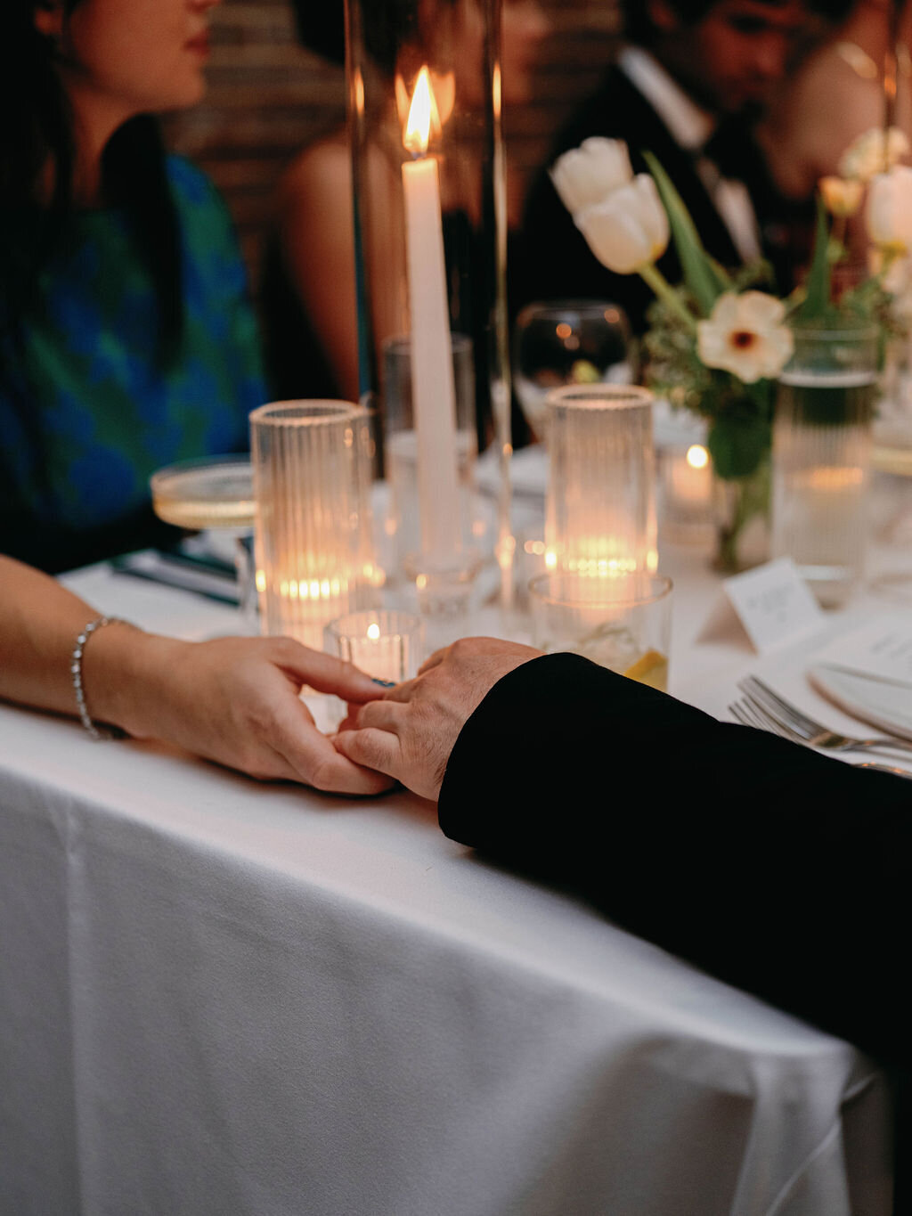 Holding hands at the table with candles and florals in the background.