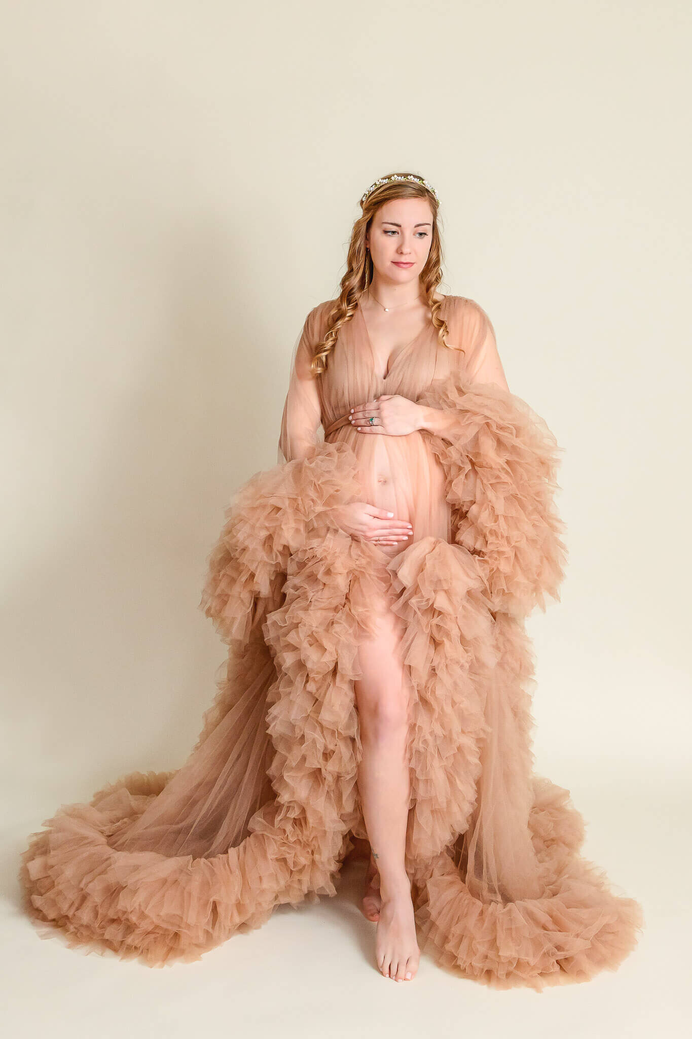 A pregnant woman wearing a tan robe and showing off her bare belly.