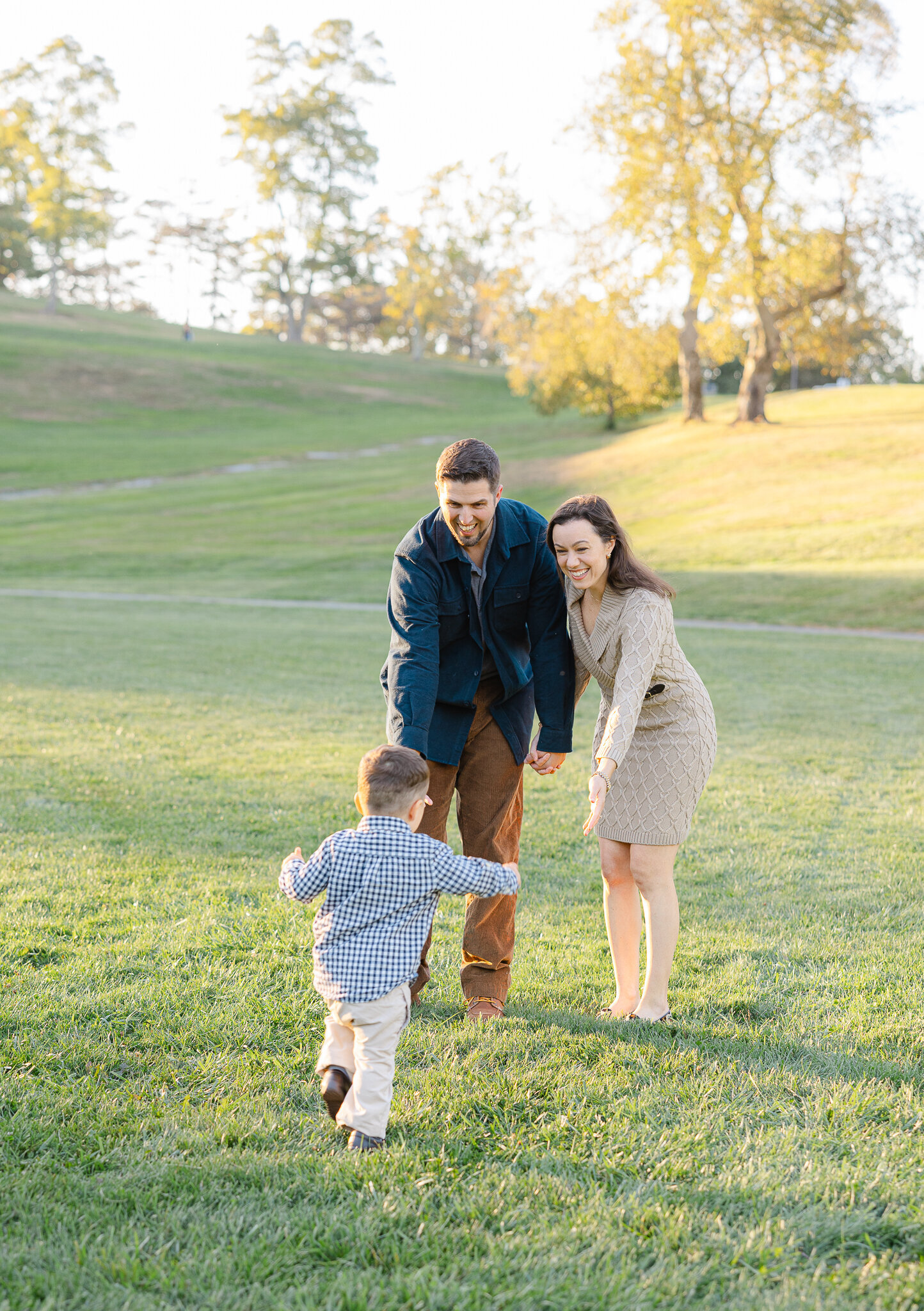 A young boy runs across a grassy field toward his smiling parents, photographed by a Worcester family photographer.