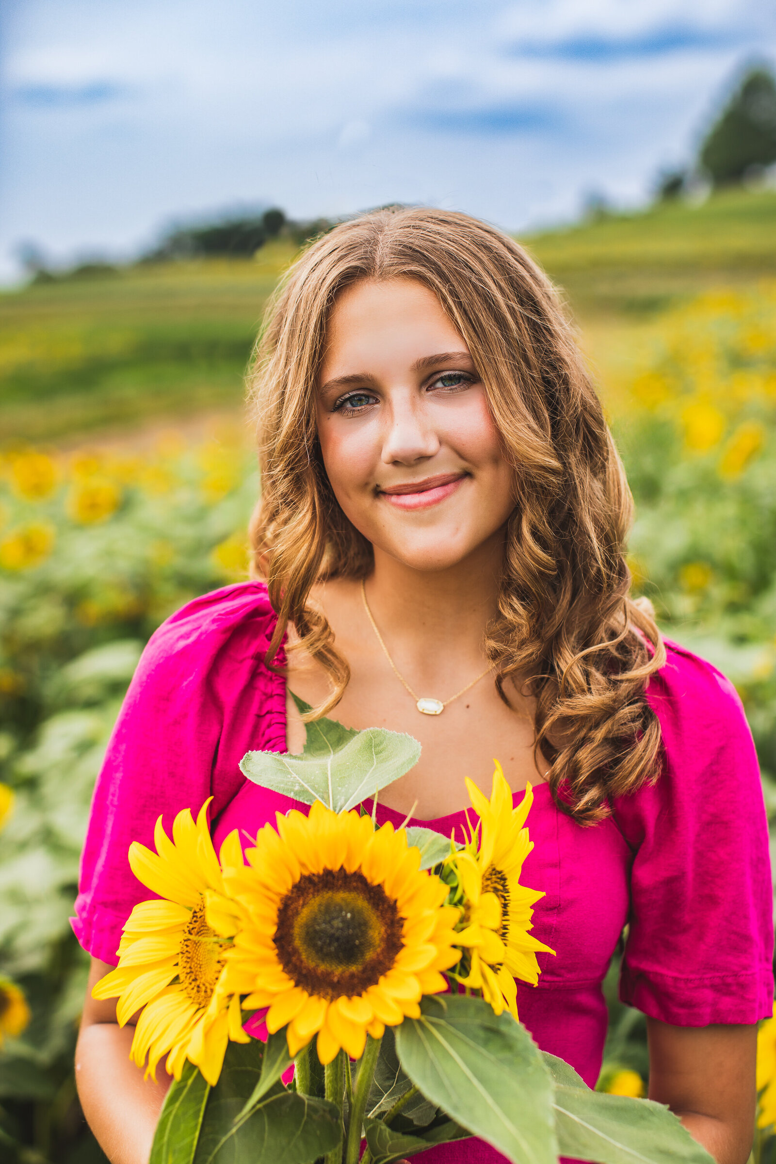 A girl in a pink dress holding a bouquet of sunflowers posing for a headshot in a sunflower field