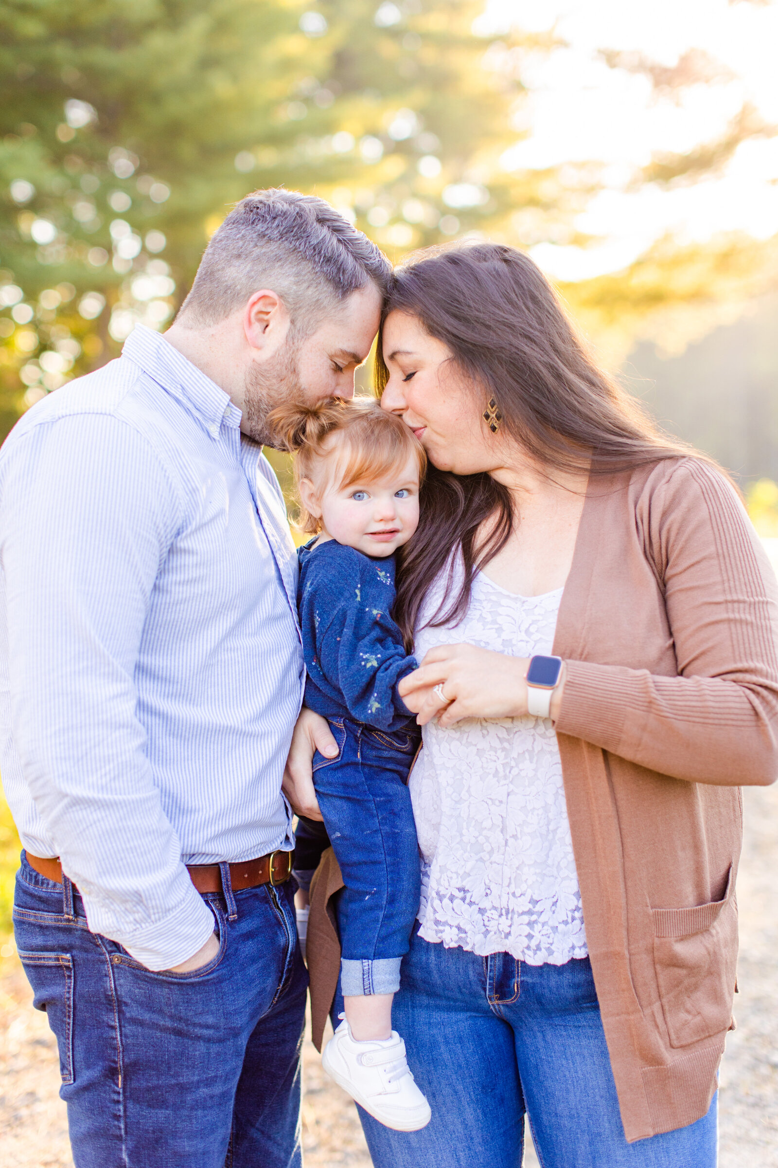 mom and dad kissing daughter on the head