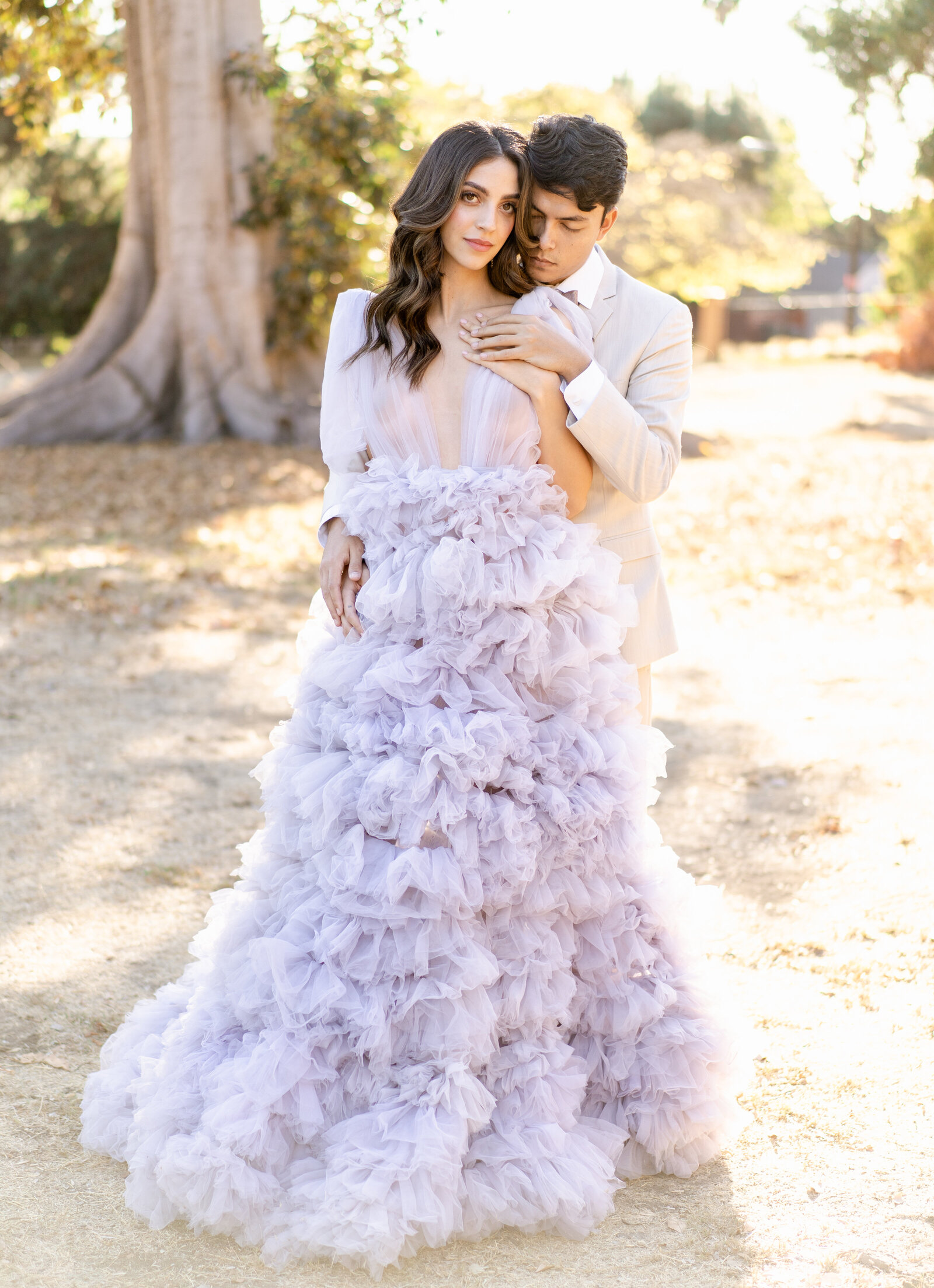 Portrait of bride and groom in a lavender wedding gown and cream suit embracing outdoors with large tree outback.