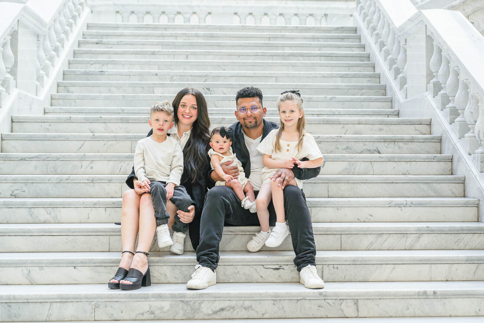 A mother, father, their young son, daughter, and baby daughter, sitting on the steps inside the Utah State Capitol. Captured by Melissa Woodruff Photography