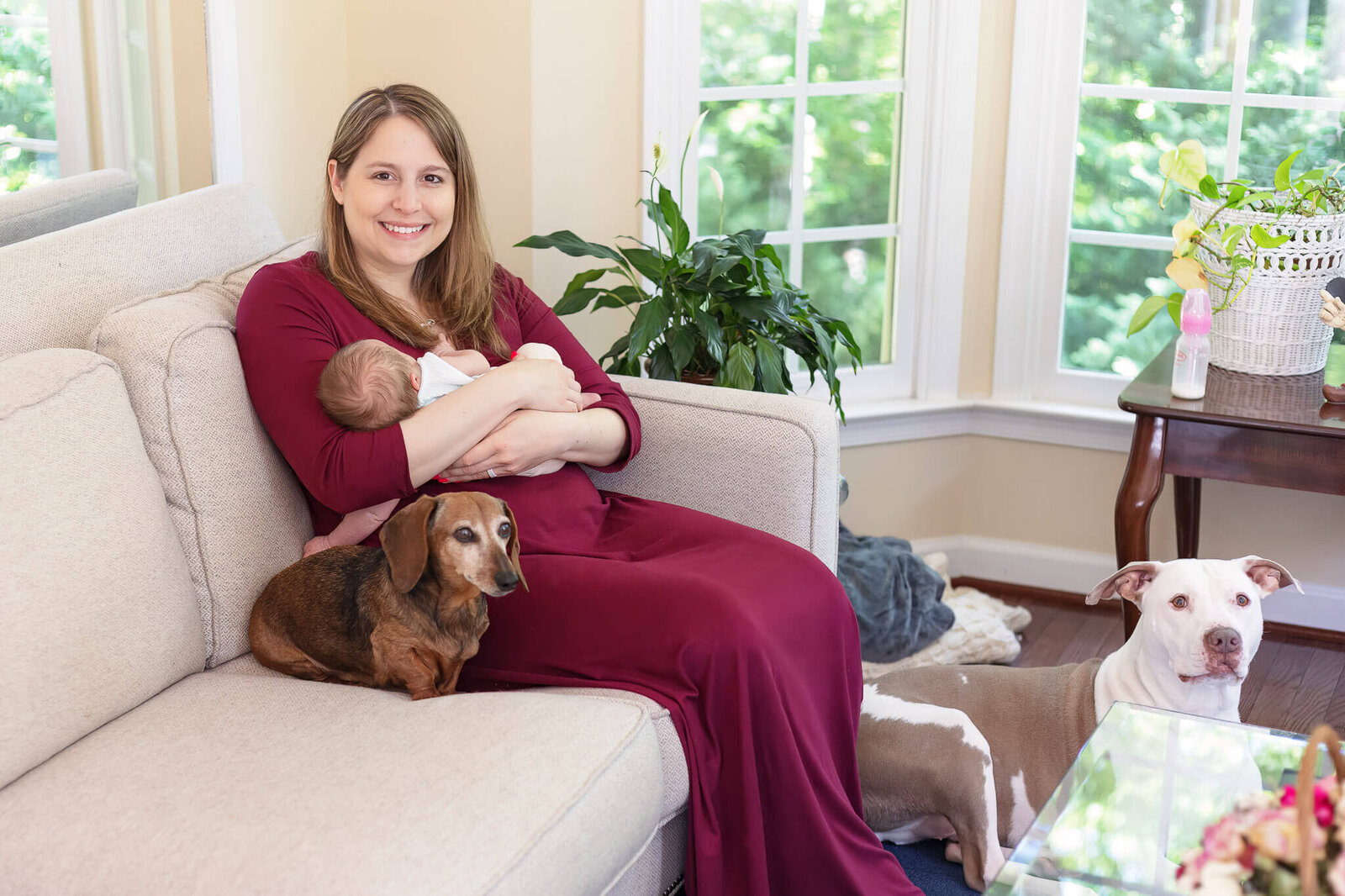 A Manassas mom holding her newborn and snuggling with her dog on the couch.