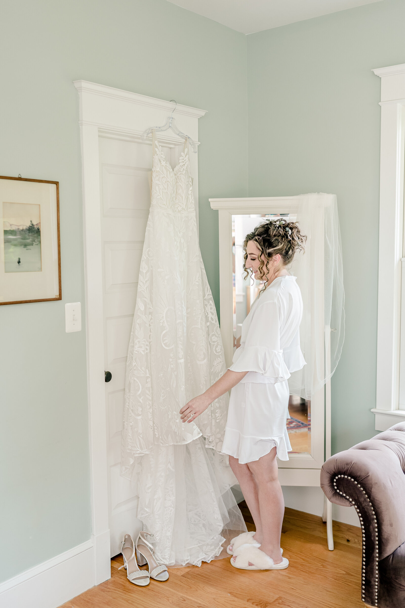 A bride dressed in a white robe and slippers looking at her dress before her wedding at Blue Hill Farm in Loudoun County