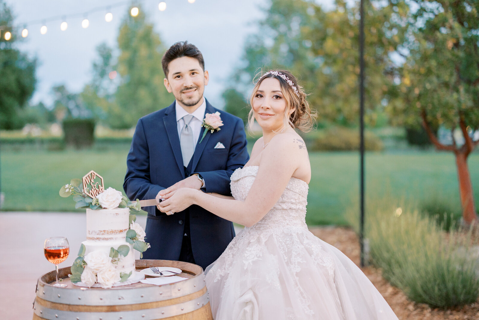 bride and groom at their outdoor reception cutting their wedding cake together under string lights captured by sacramento wedding photographer at Wolfe Heights wedding venue