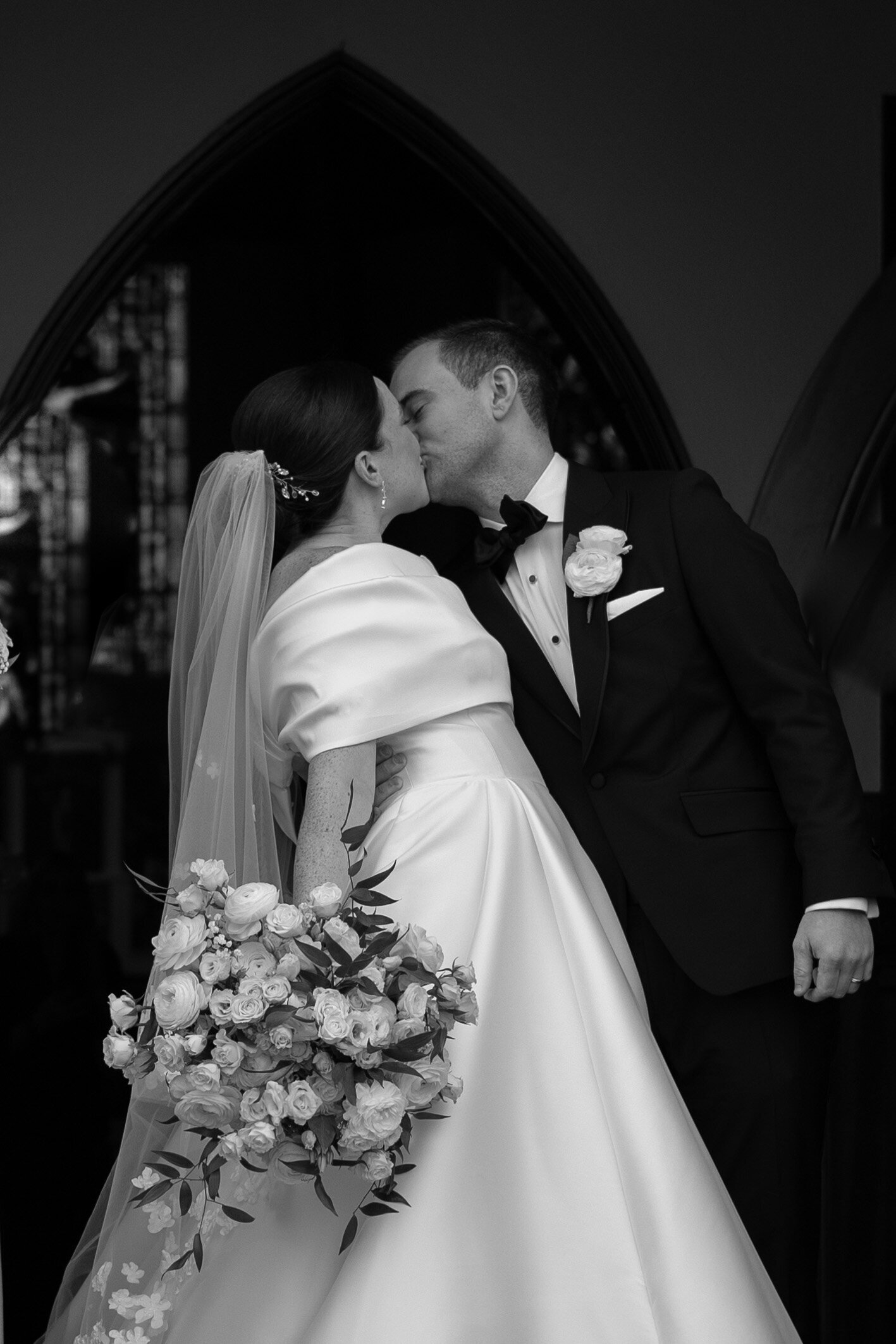 Black and white photo of groom and bride kissing outside of the chapel | Emma LeeAnn Photography