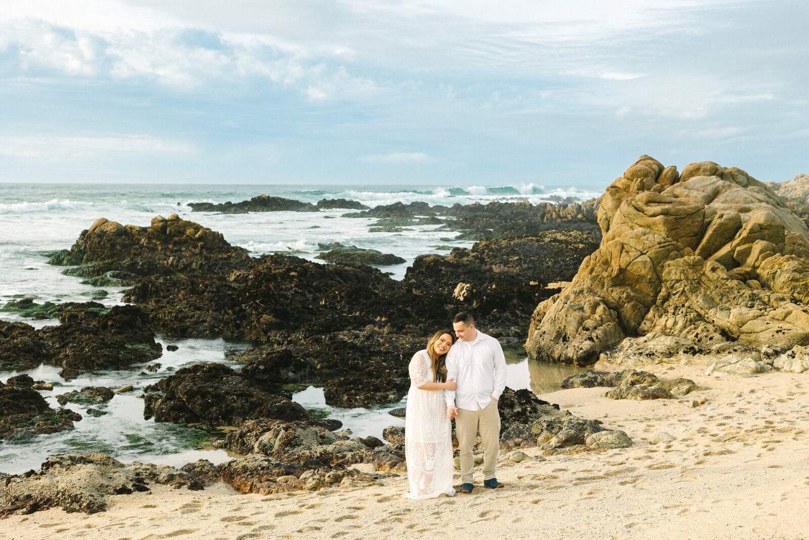 An engaged man and woman take photos on the beach in Pacific Grove, Monterey, California near Big Sur.
