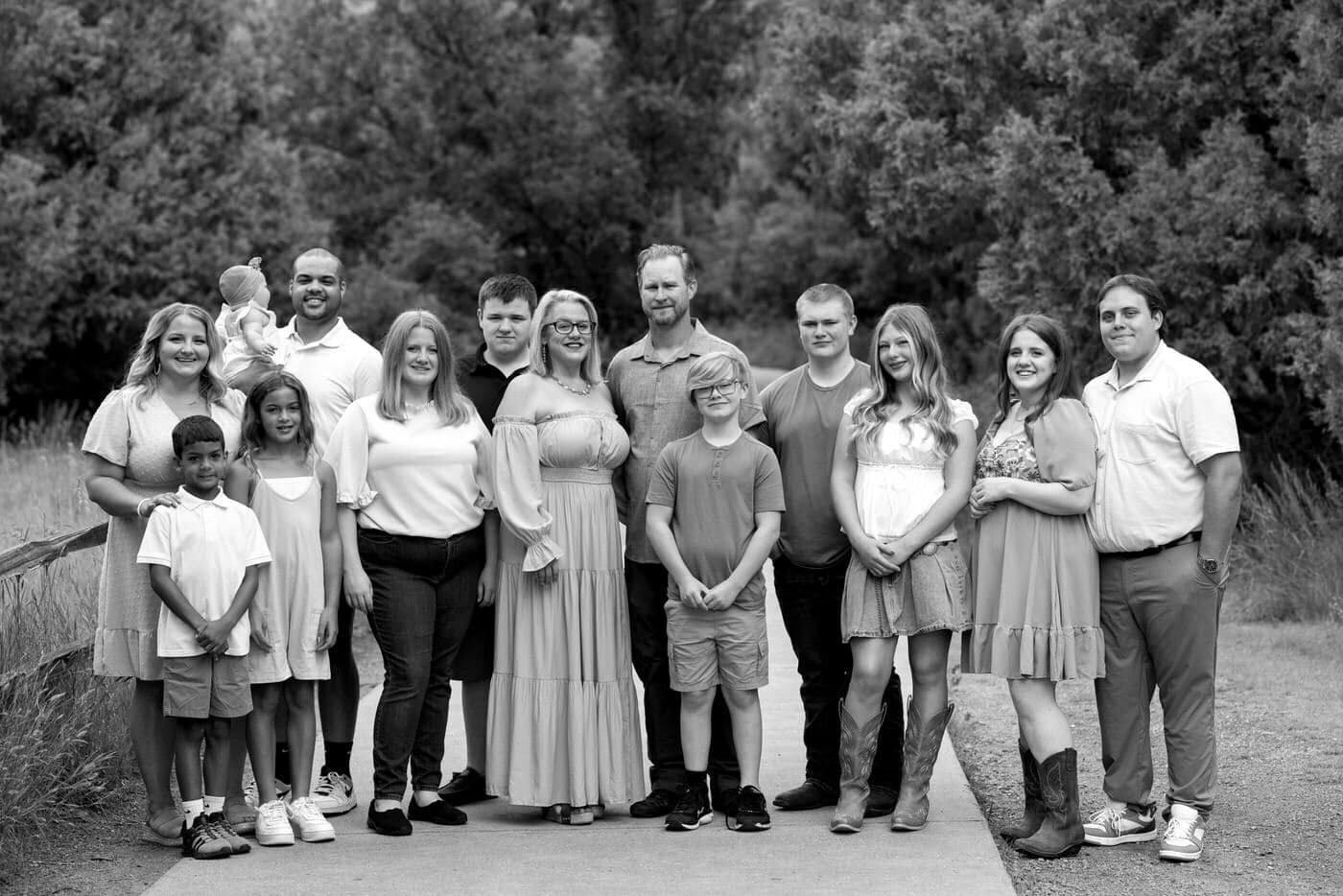 An extended family stand and pose for a big family portrait with trees behind them. 