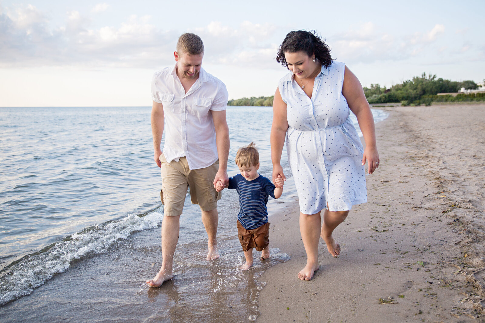 family with small boy walking along water at the beach