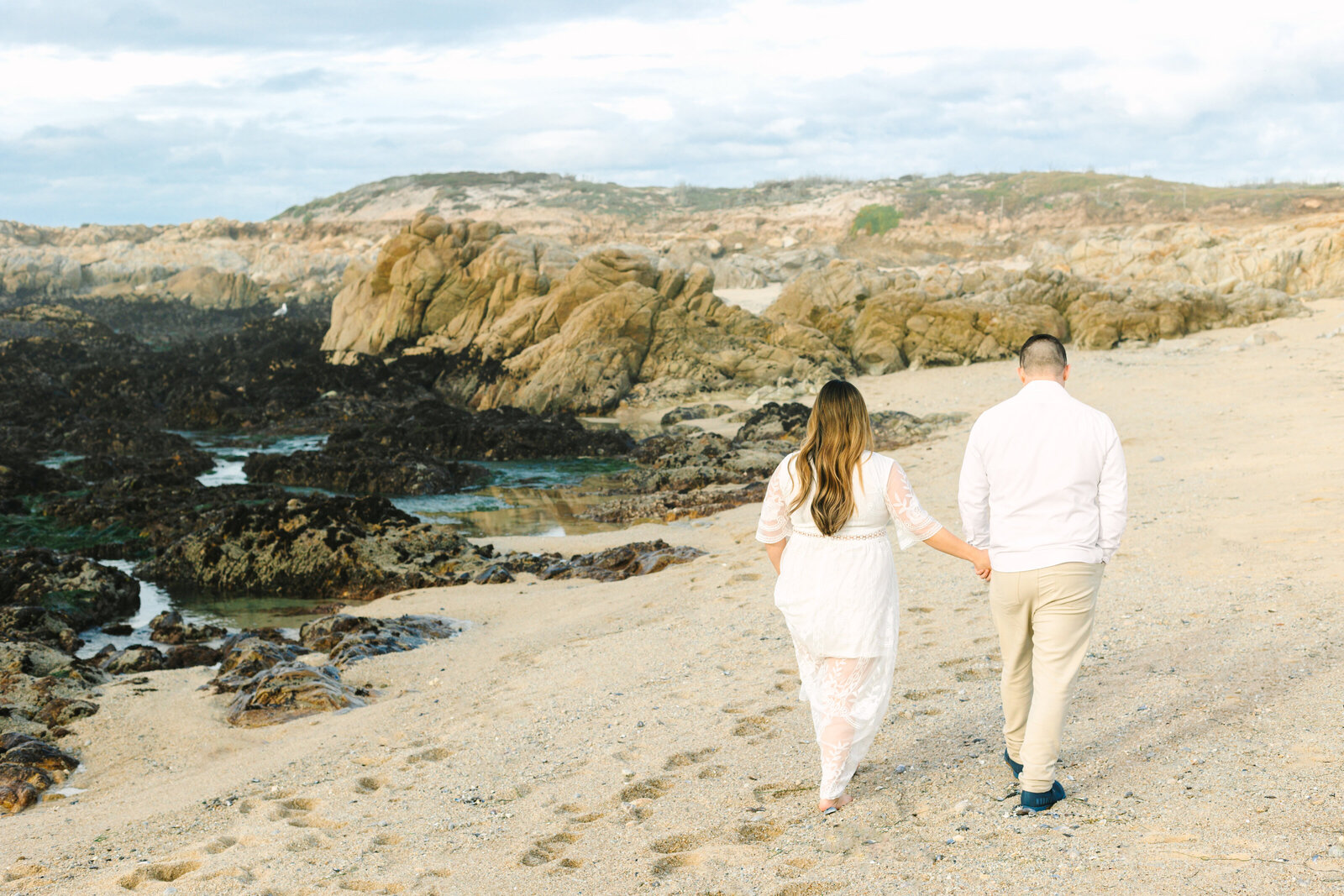 An engaged man and woman take photos on the beach in Pacific Grove, Monterey, California near Big Sur.