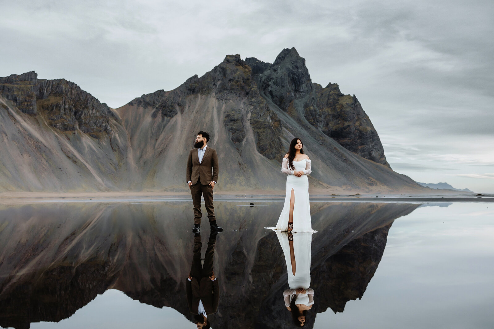 Married couple in their wedding attire standing in front of the Vestrahorn mountain on the reflective water in Iceland on their wedding day