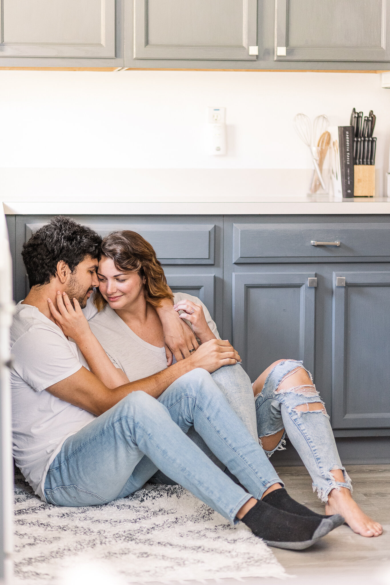 A man and woman sit on a kitchen floor snuggled up