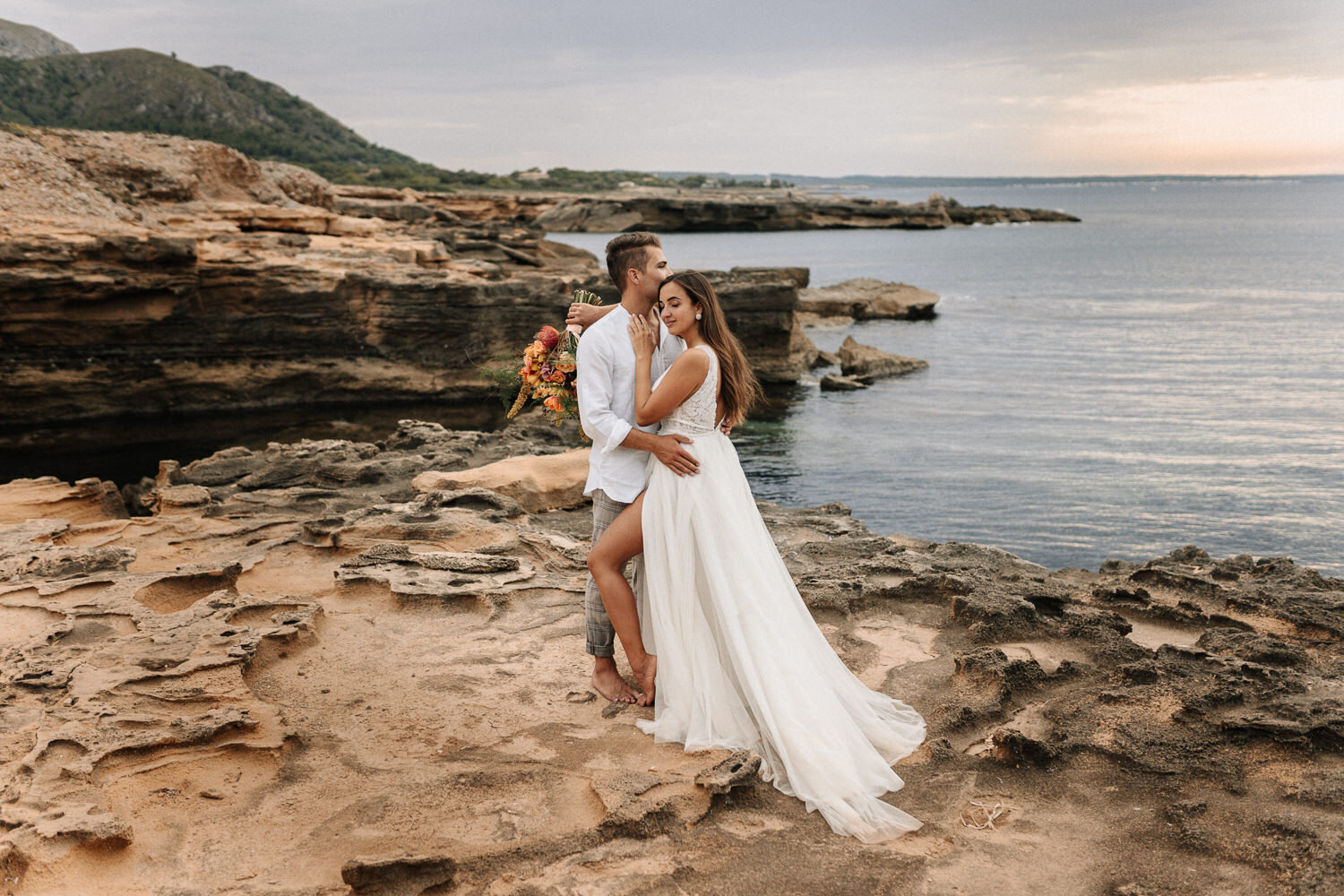 Brautpaar steht auf Klippen an der Küste von Mallorca